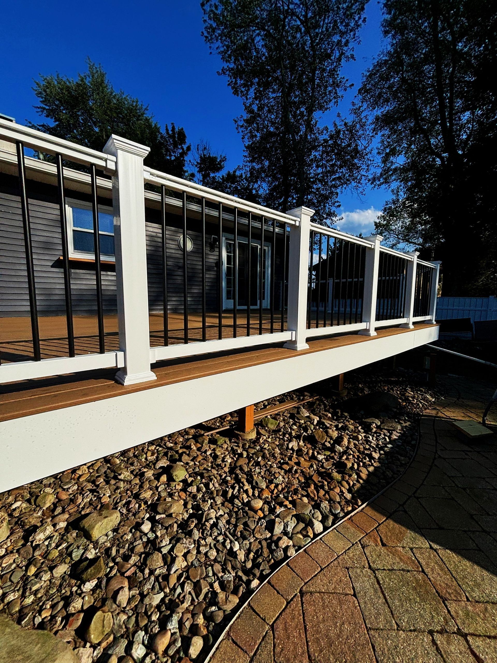 A white fence surrounds a wooden deck in front of a house