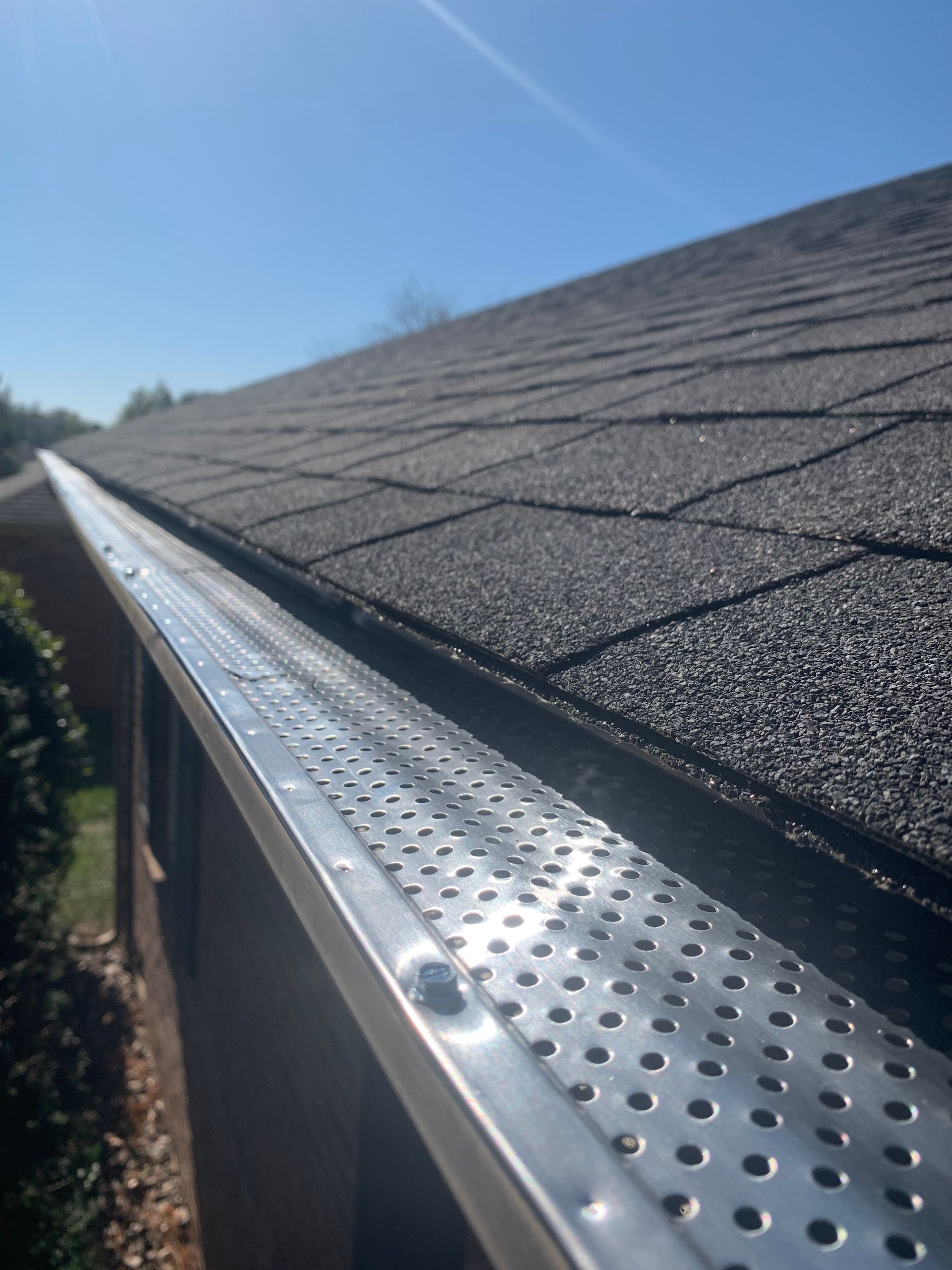 Close-up of a roof edge with shiny metal gutter guard under sunlight against a clear blue sky