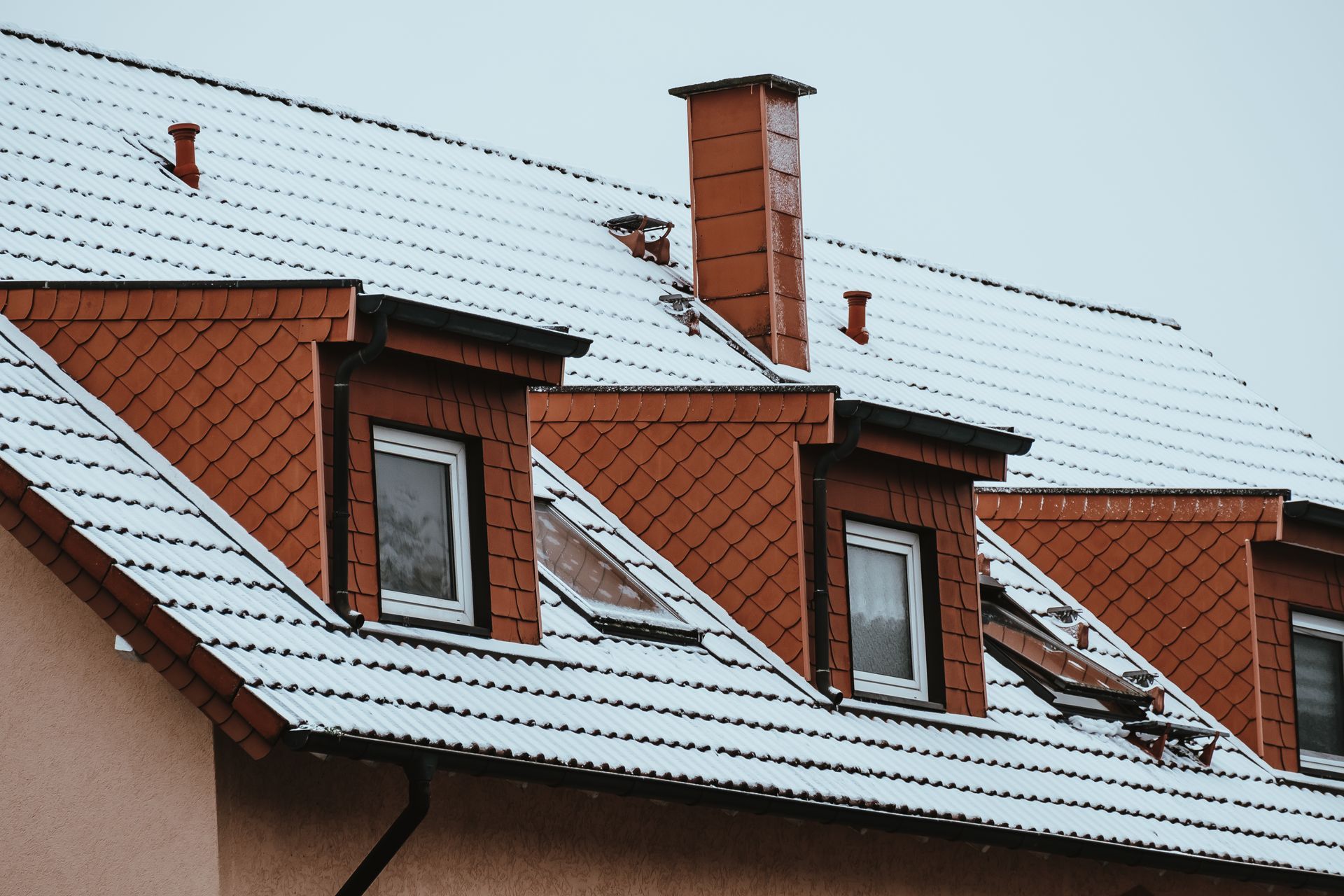 Snow-covered red brick house roof with dormer windows and a chimney