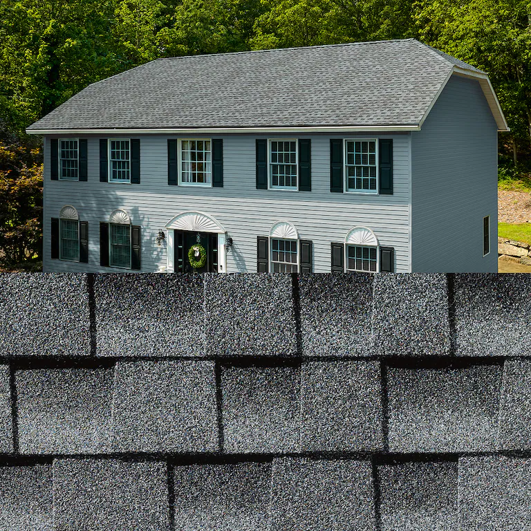 Gray two-story house above close-up of dark gray asphalt shingles.