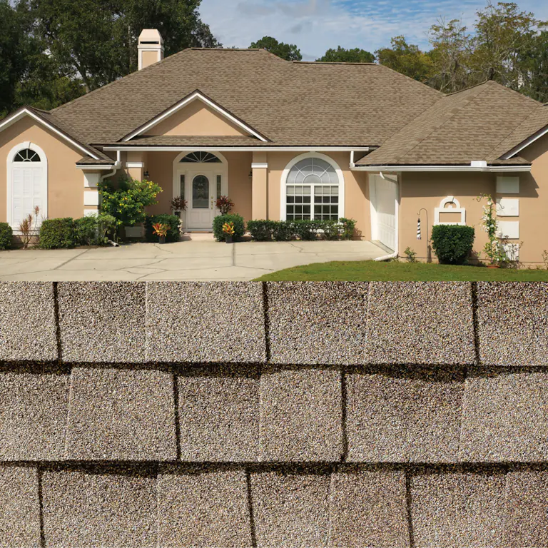 Suburban beige house with a tan shingle roof behind a textured gray stone wall