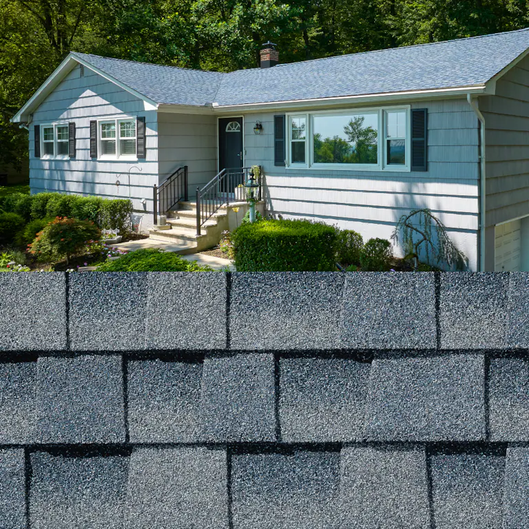 Single-story light blue house with gray roof and front steps, shown behind stacked gray asphalt shingles