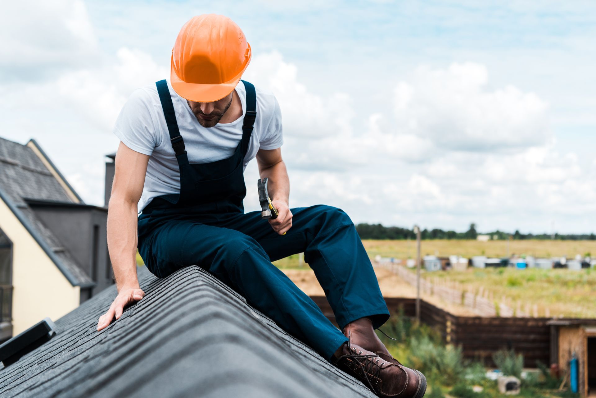 Worker in orange hard hat sitting on a rooftop, inspecting the roof edge.