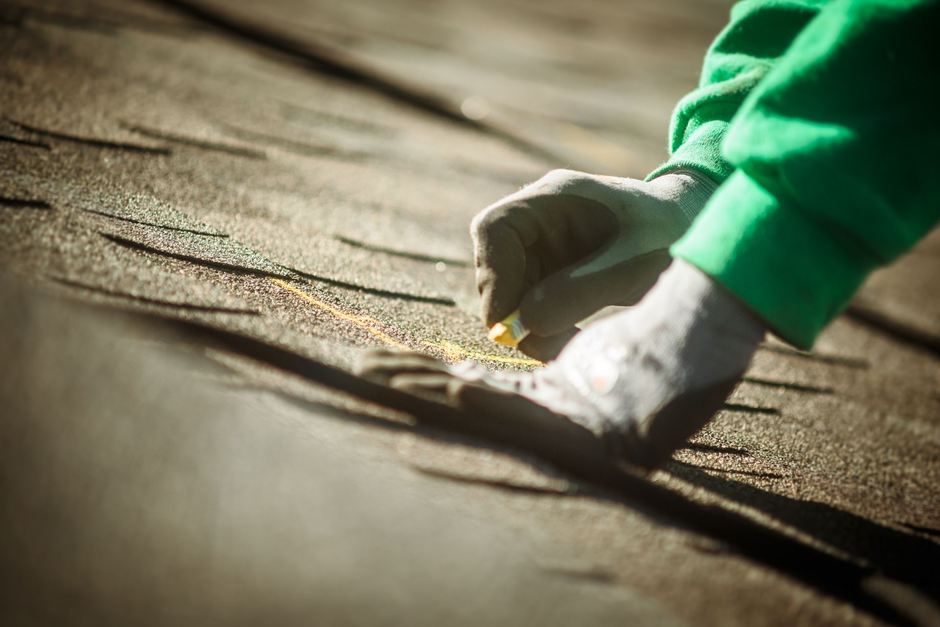 Gloved hands sprinkling granules onto a shingled roof during repairs