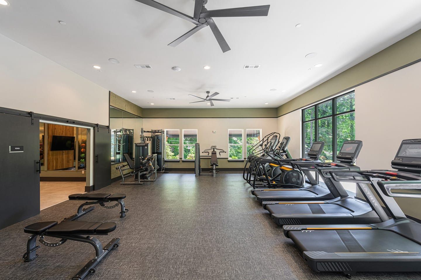 A gym with a lot of treadmills and a ceiling fan