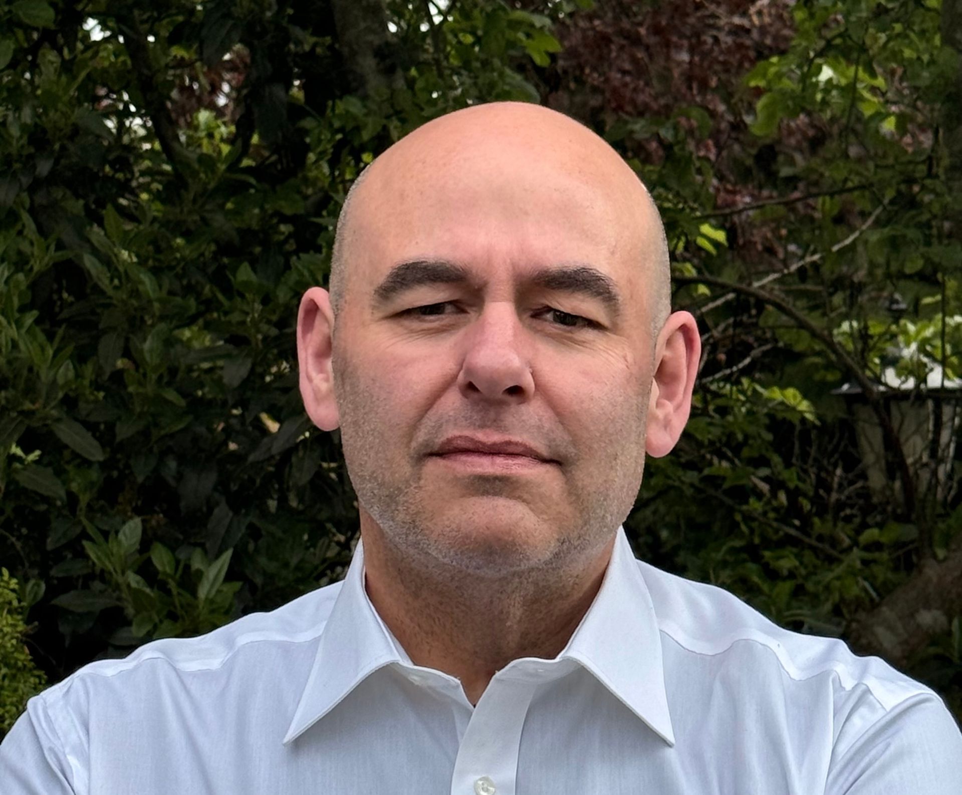 A bald man with a beard and a purple shirt is looking at the camera.
