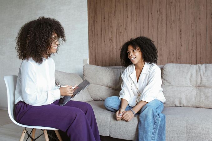 Two women are sitting on a couch using laptops.