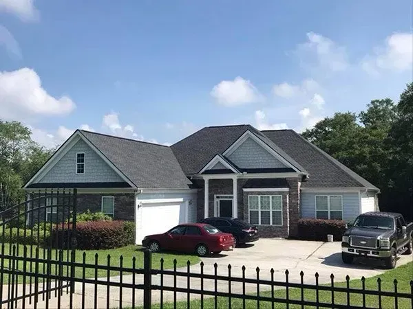 A single-story brick house with a gray roof and light blue siding, featuring a driveway with two parked cars.