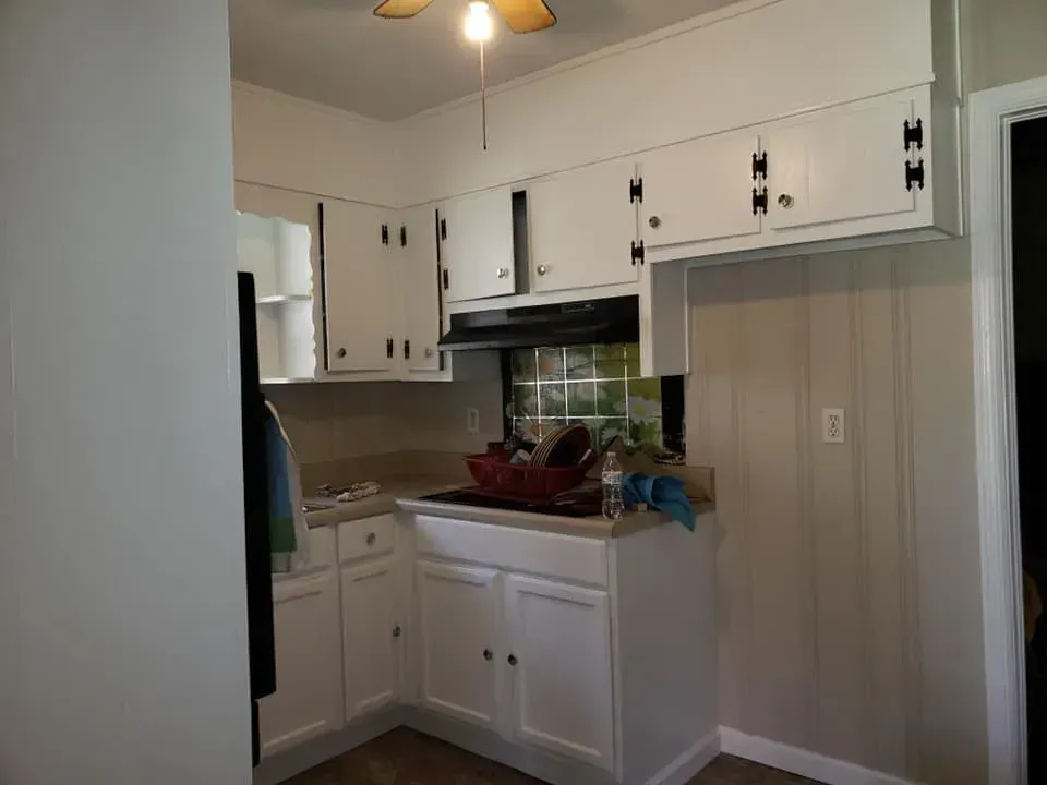 A kitchen corner featuring white cabinets, a small countertop, and a dark vent hood above a stove area.