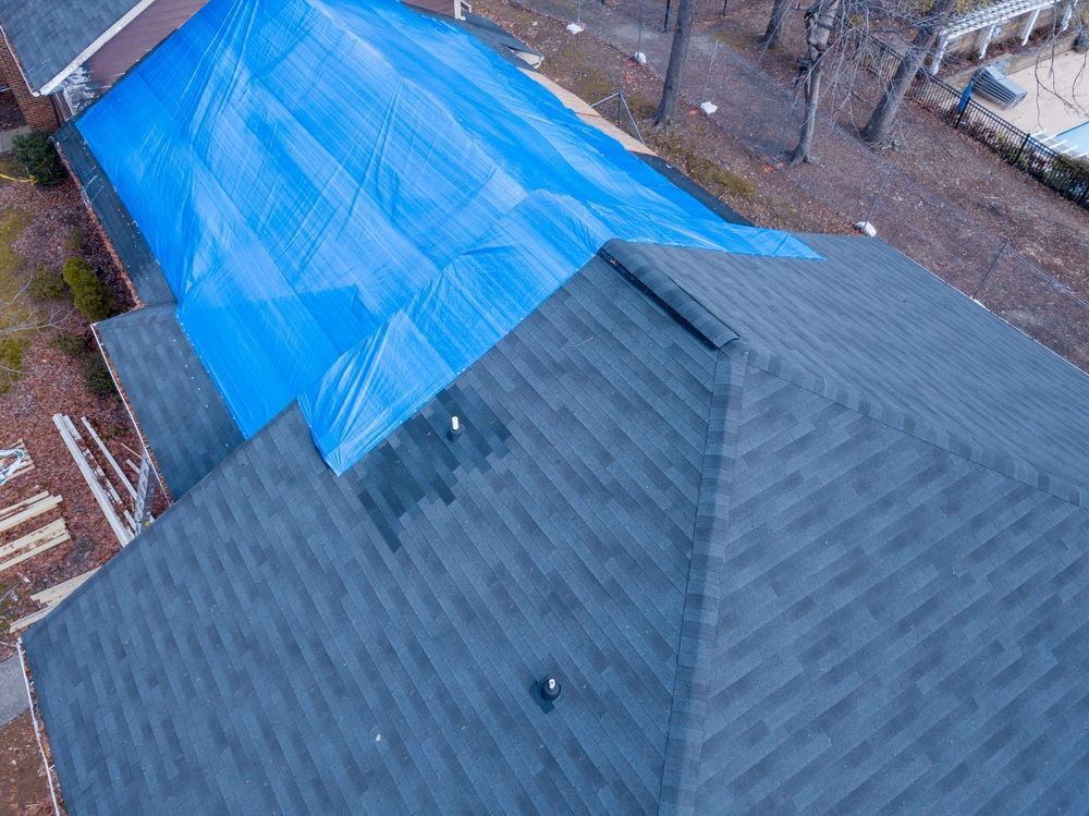 An aerial view of a shingled residential roof with a large blue tarp covering one side, likely for temporary repairs.