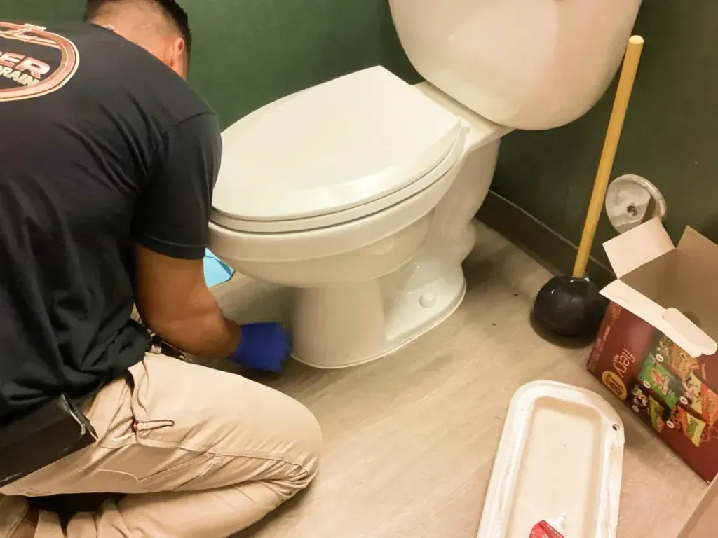 Person installing a bidet attachment on a white toilet in a bathroom.