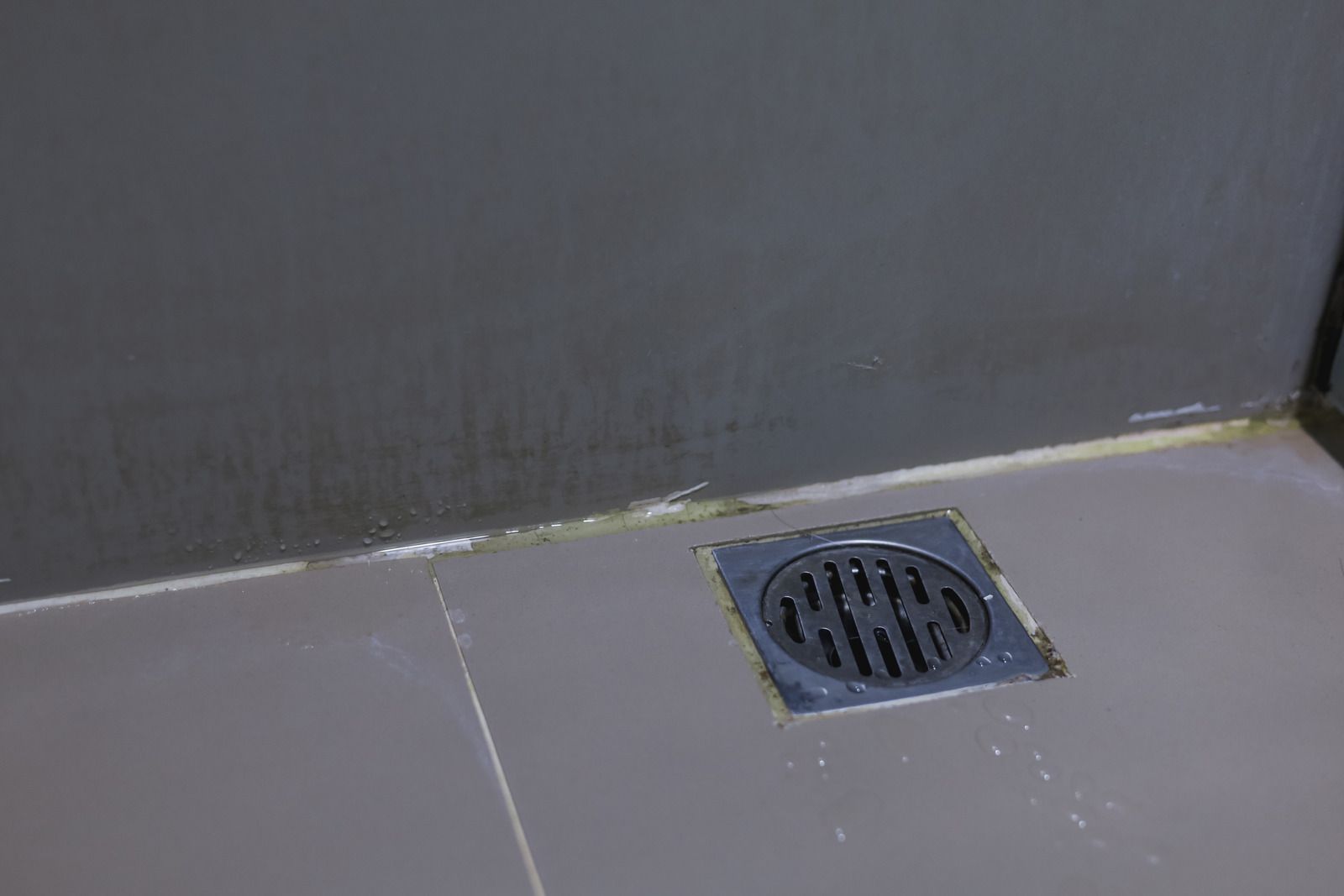 Floor drain near a gray wall on tiled flooring
