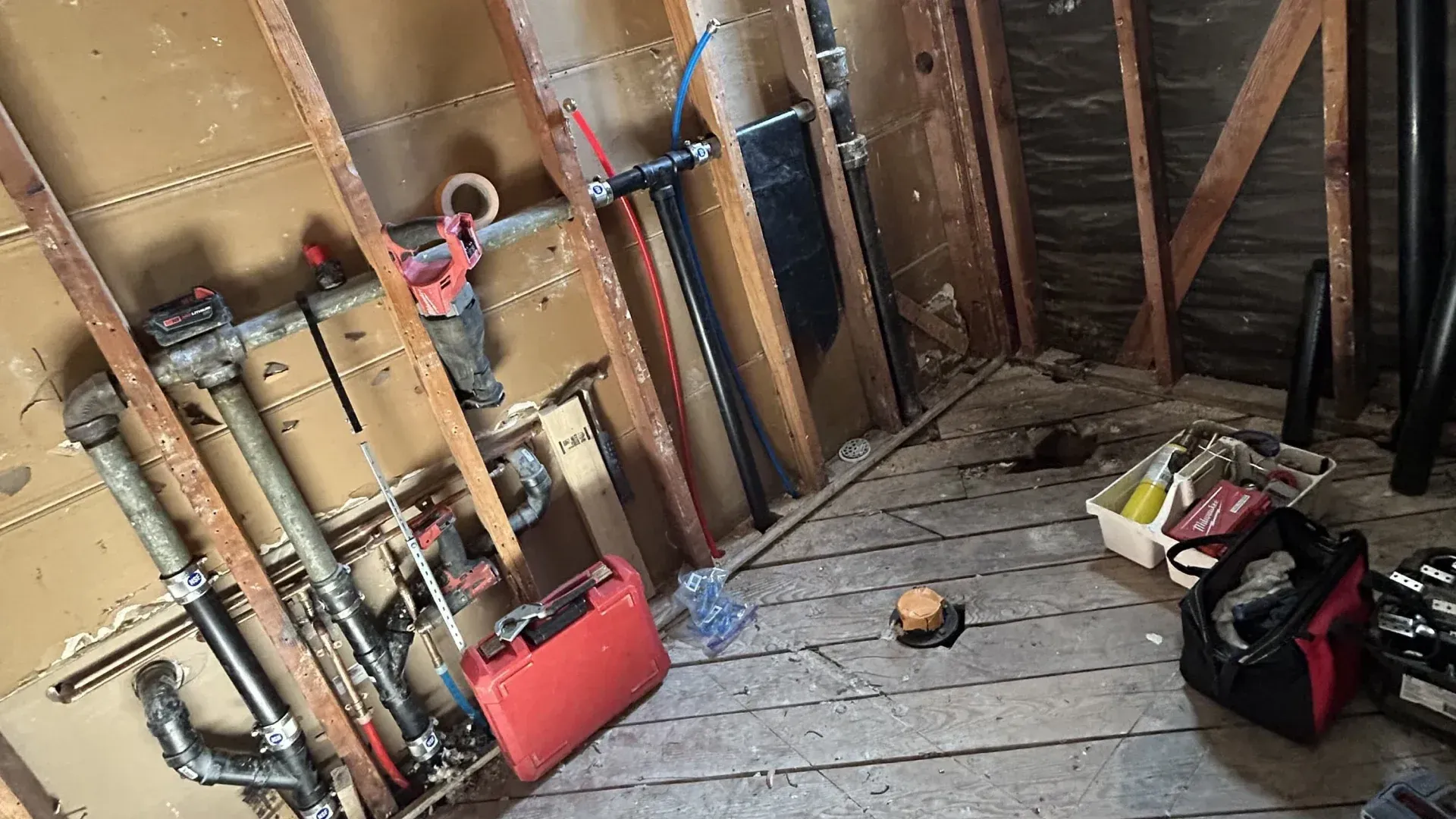 Cluttered attic with exposed insulation, wooden beams, tools, and debris on the floor