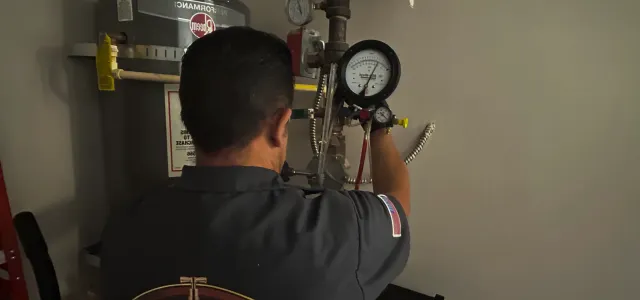 Person adjusting a pressure gauge on industrial pipes in a utility room