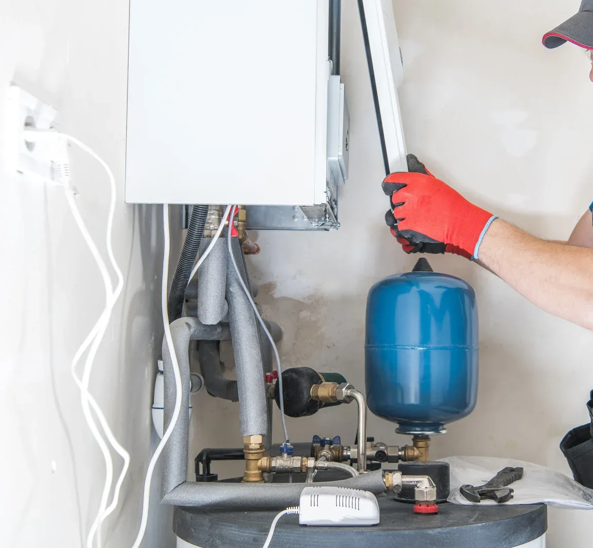 Technician in red gloves repairing a boiler and blue expansion tank with tools in a utility room