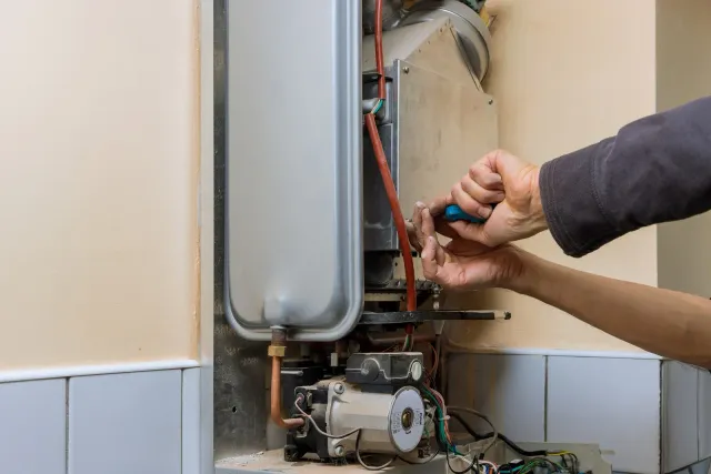 Technician repairing a wall-mounted boiler with a screwdriver and wrench in a tiled room