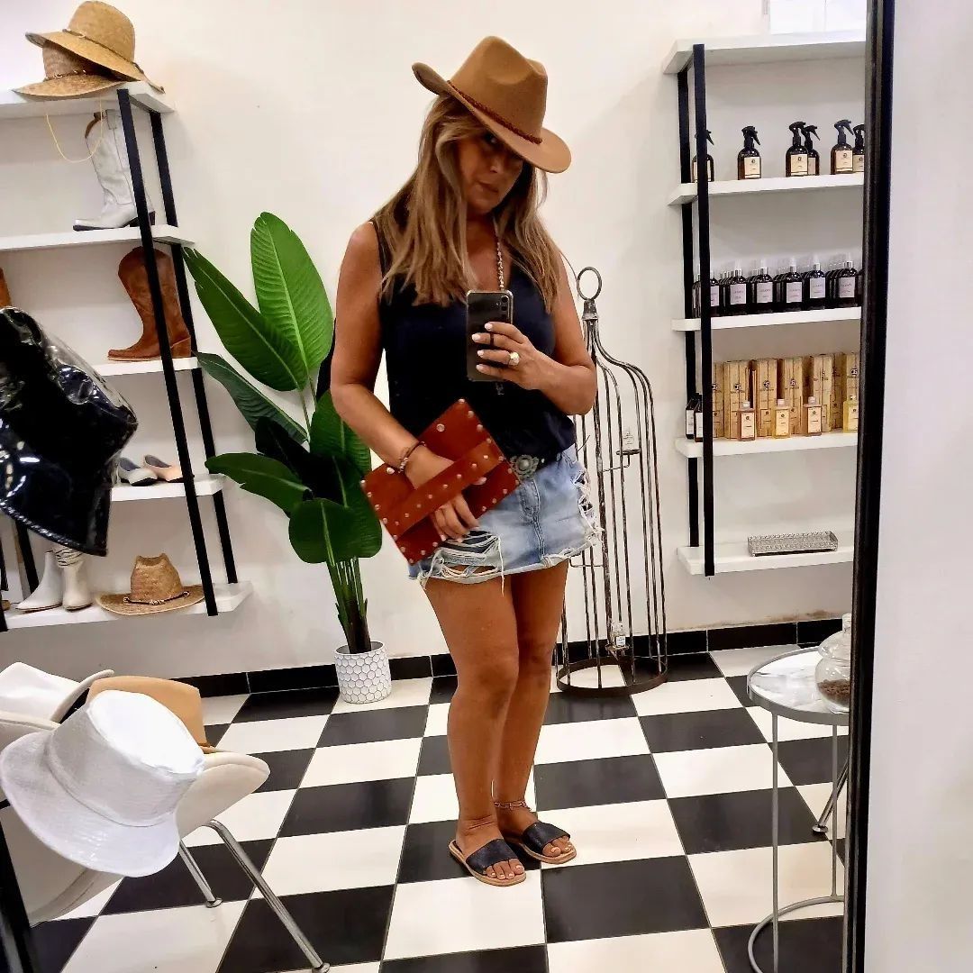 Mujer con sombrero tomándose una selfie frente al espejo en una boutique con piso de baldosas a cuadros blancas y negras.