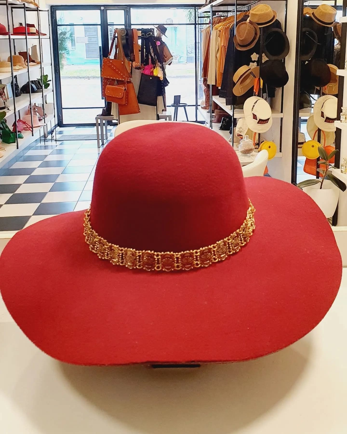 Sombrero rojo de ala ancha con ribete dorado expuesto en el mostrador de una sombrerería.