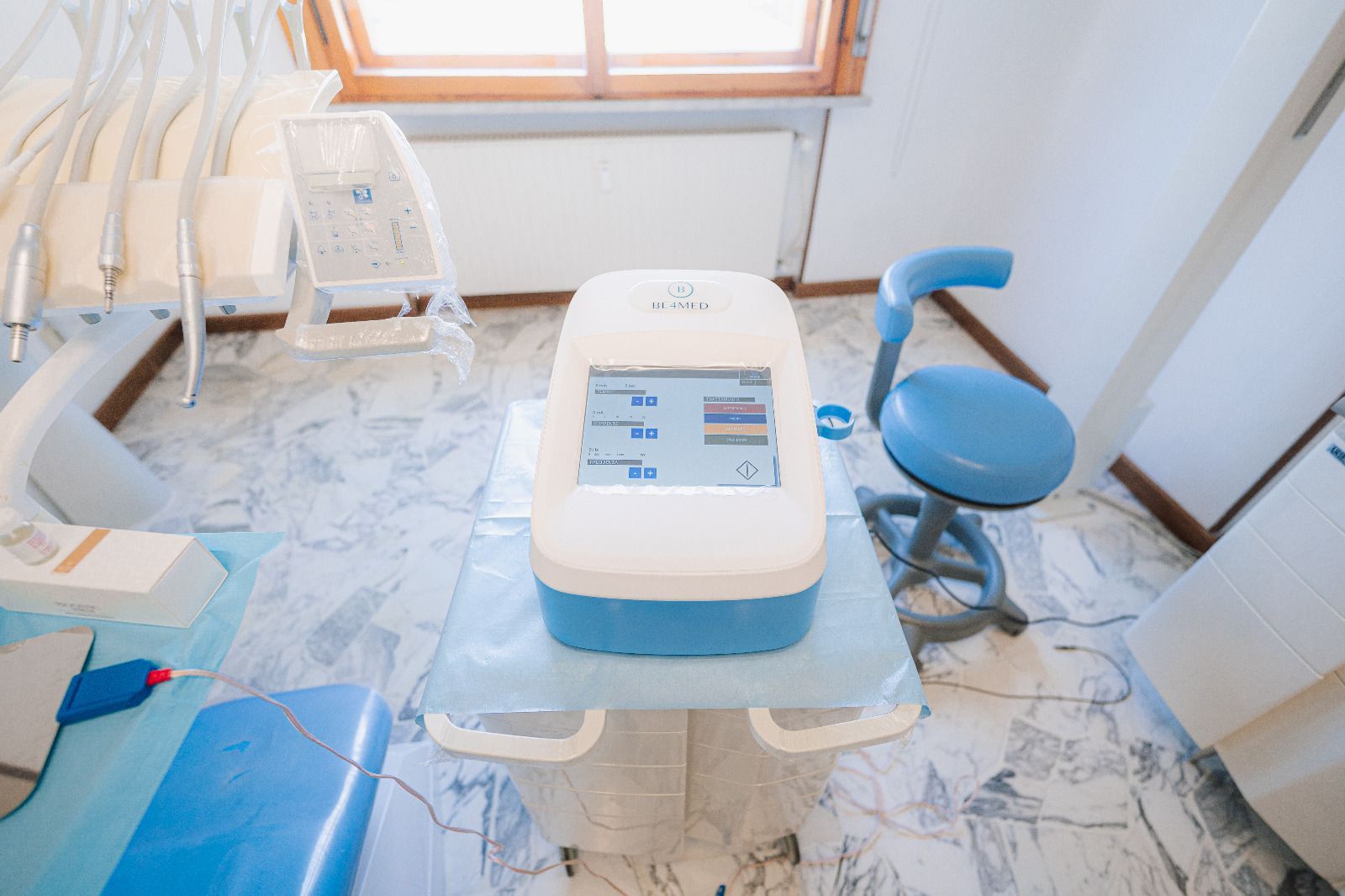 Clinica dentistica moderna con poltrona turchese e bianca, piante colorate e cartello alla reception con la scritta 
