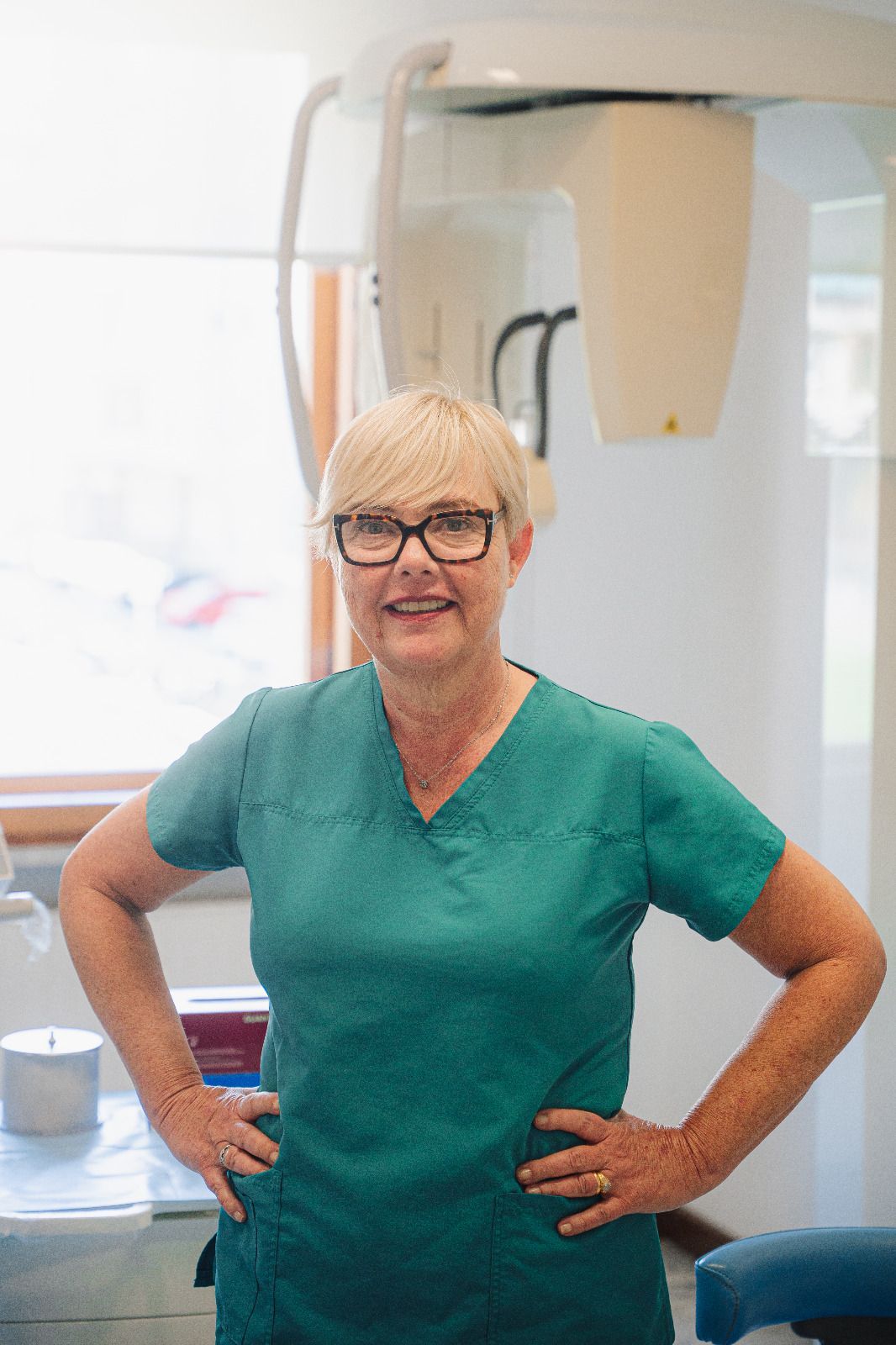 Persona sorridente in camice verde in piedi con le mani sui fianchi in uno studio dentistico
