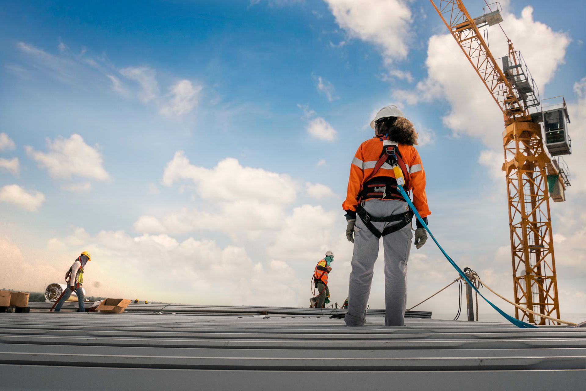 Roofing contractors working safely on a commercial metal roof with harnesses and safety gear.