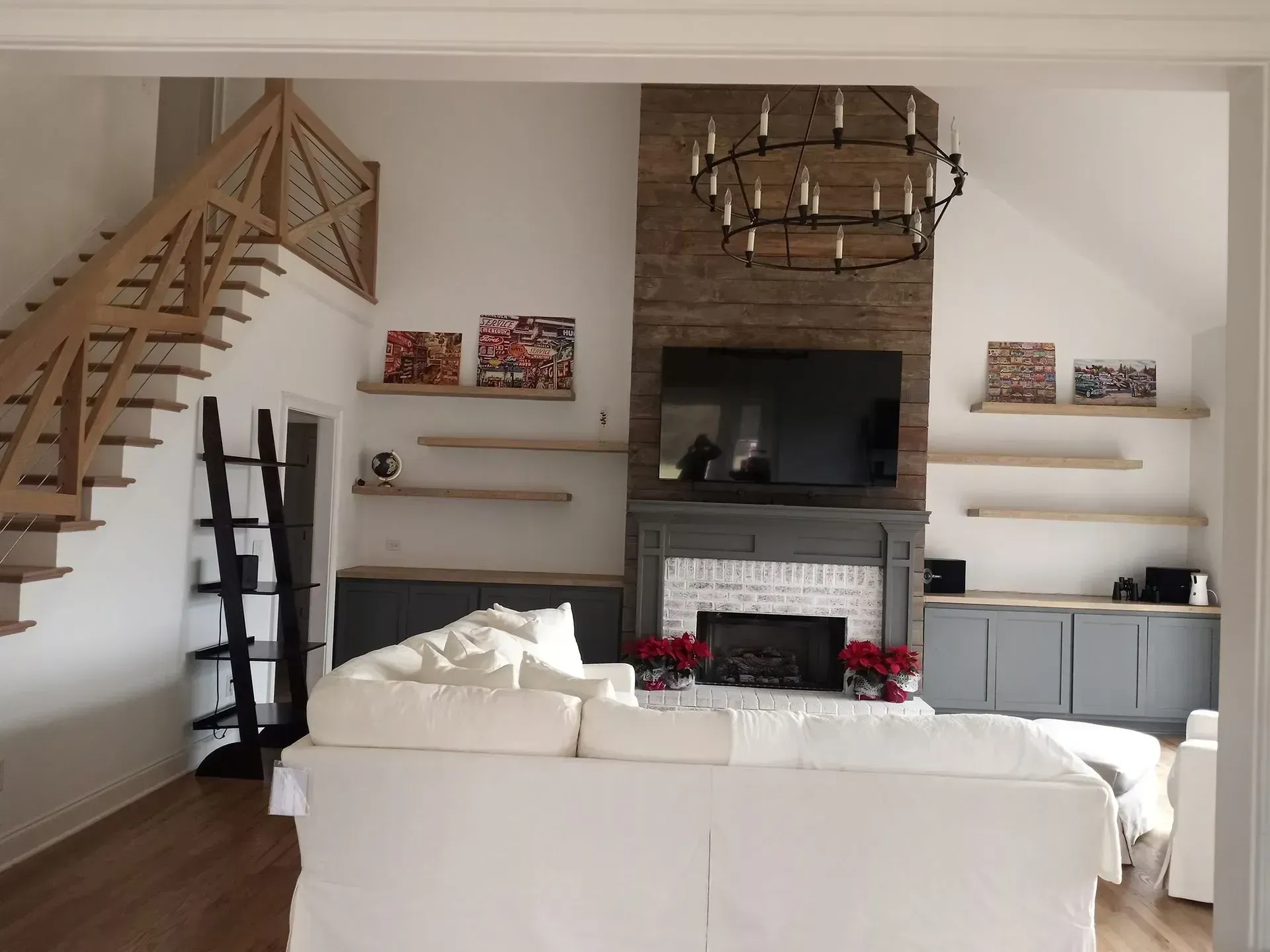 Modern living room with white sofa, fireplace, floating shelves, and wooden staircase