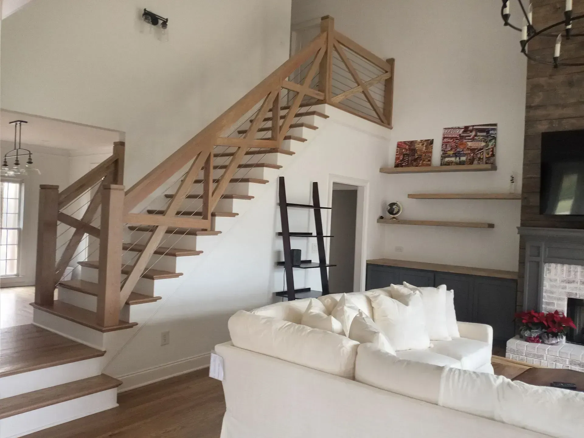 Living room with wooden staircase, white sofa, fireplace, and shelves on a beige wall.