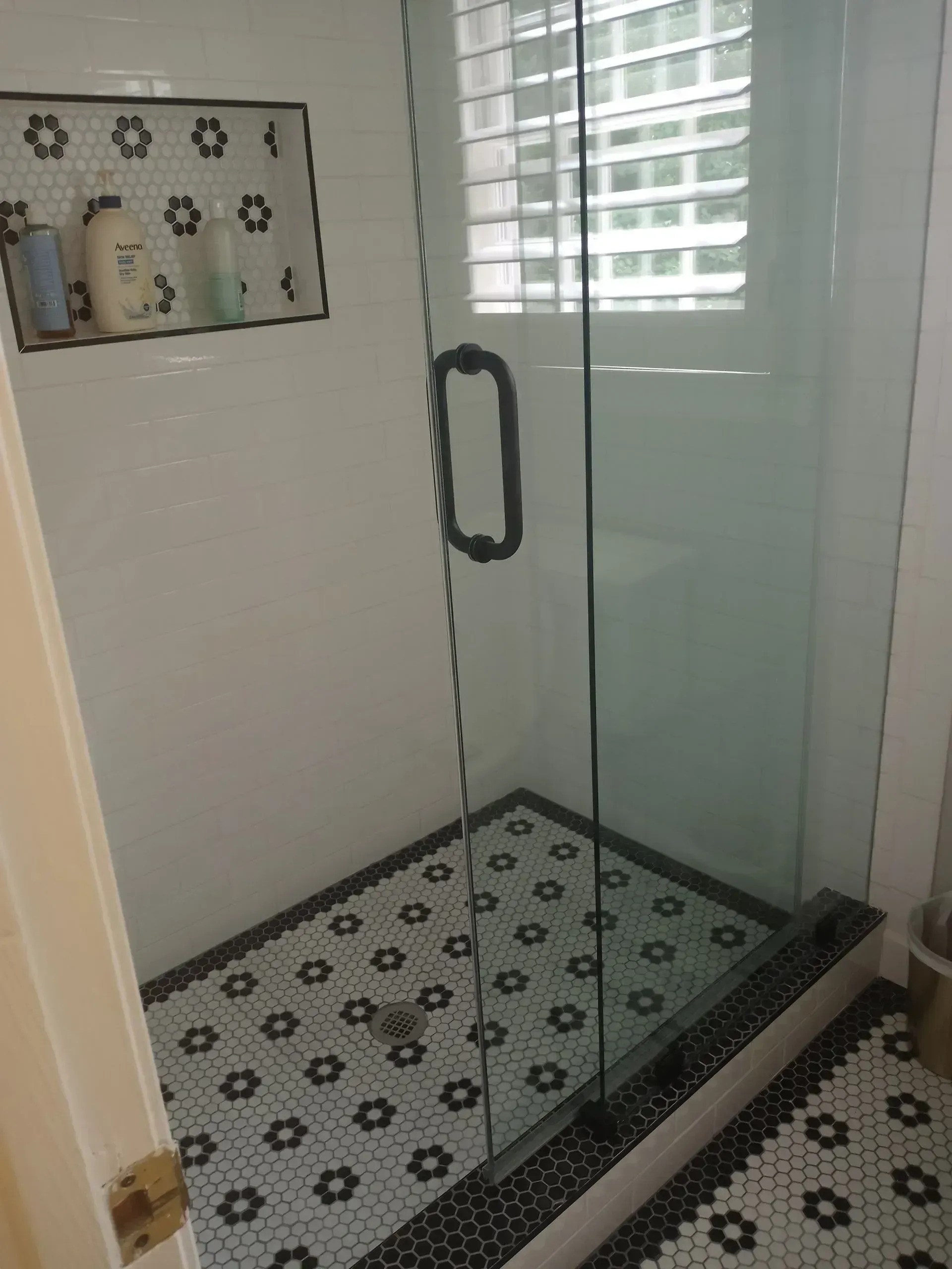 Modern glass shower enclosure with patterned tile floor and white walls