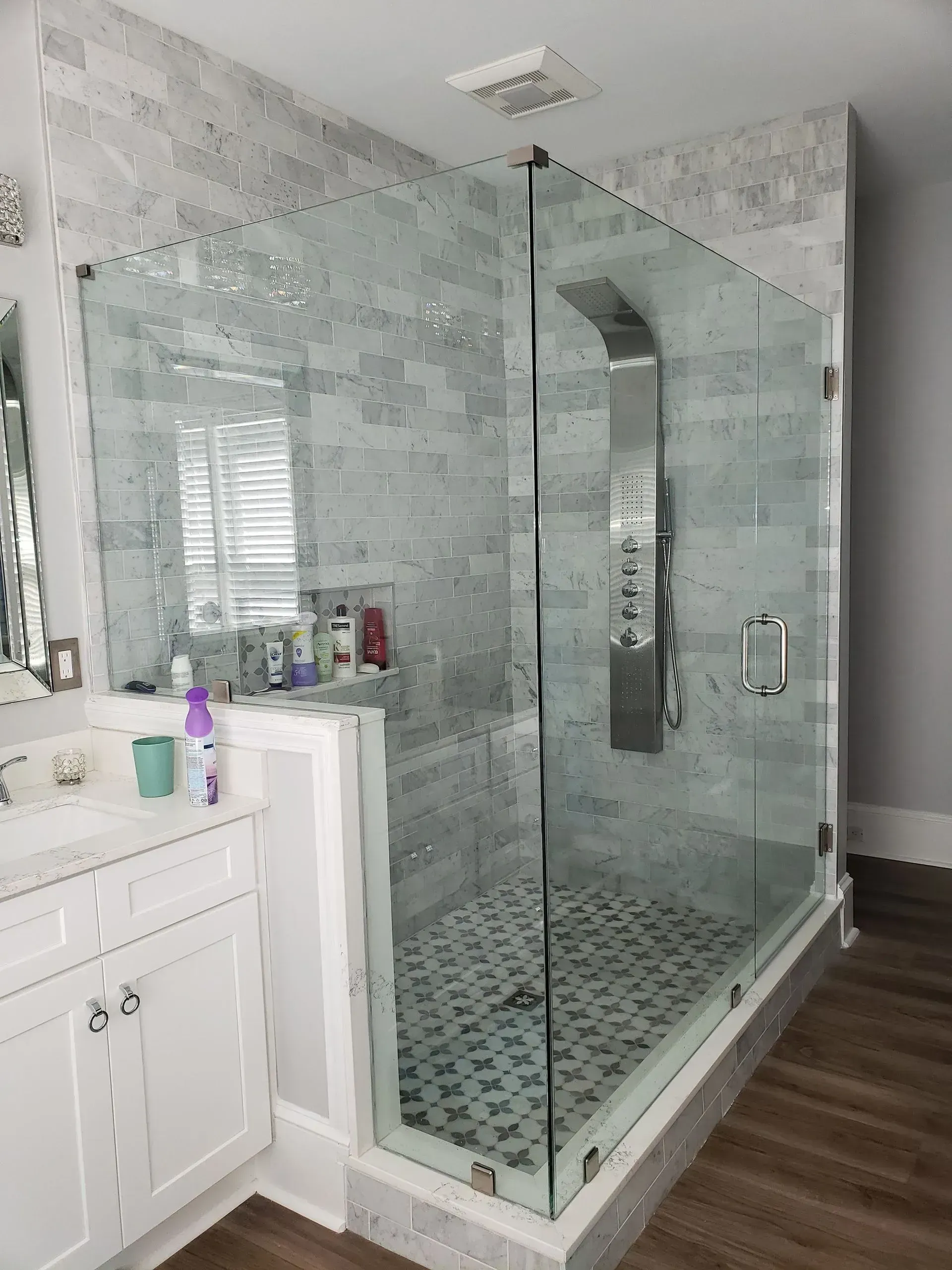 Glass walk-in shower with gray tile and mosaic floor in a bathroom