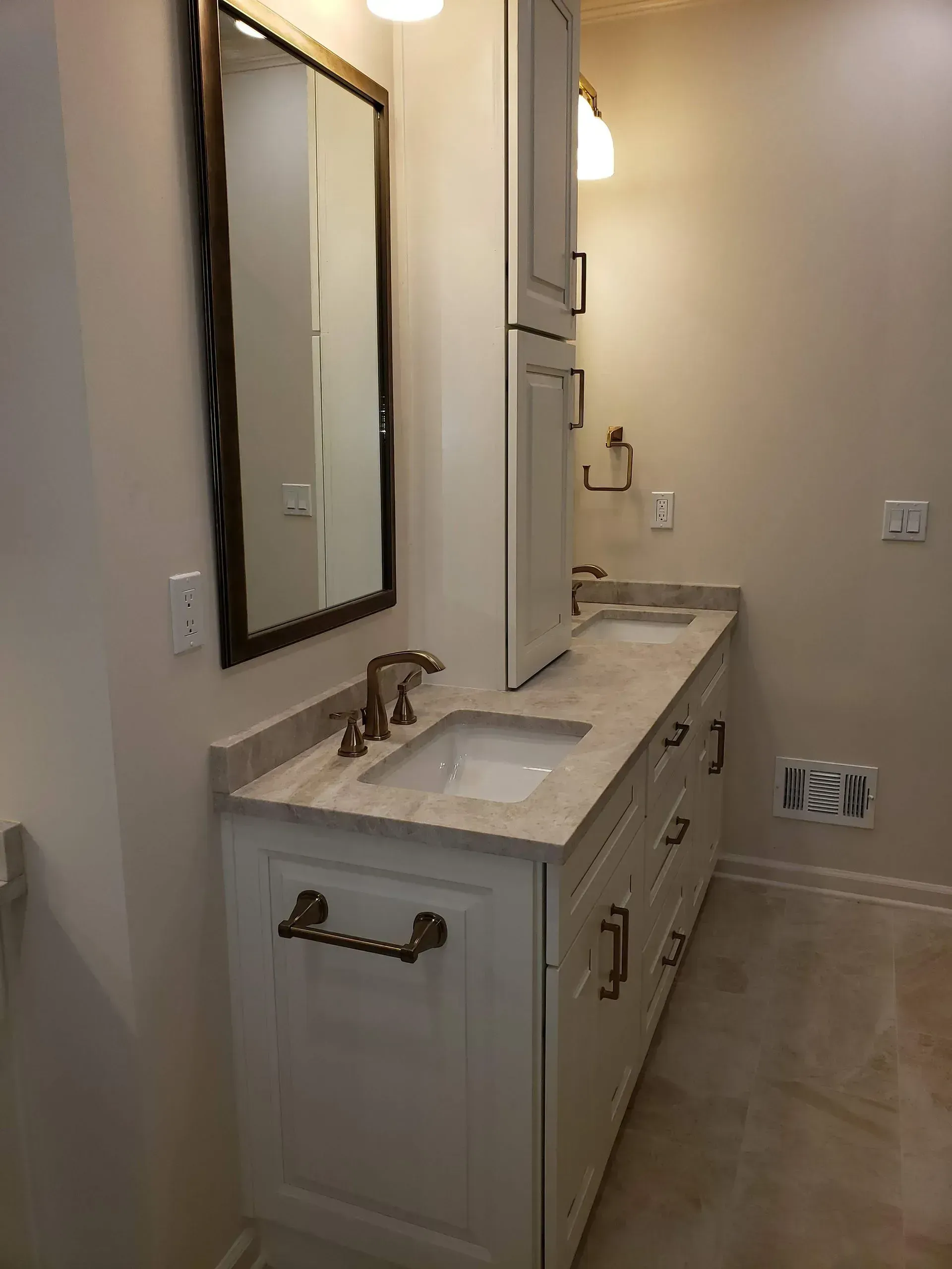 Bathroom vanity with double sinks, large mirror, and light-colored cabinets in a narrow room