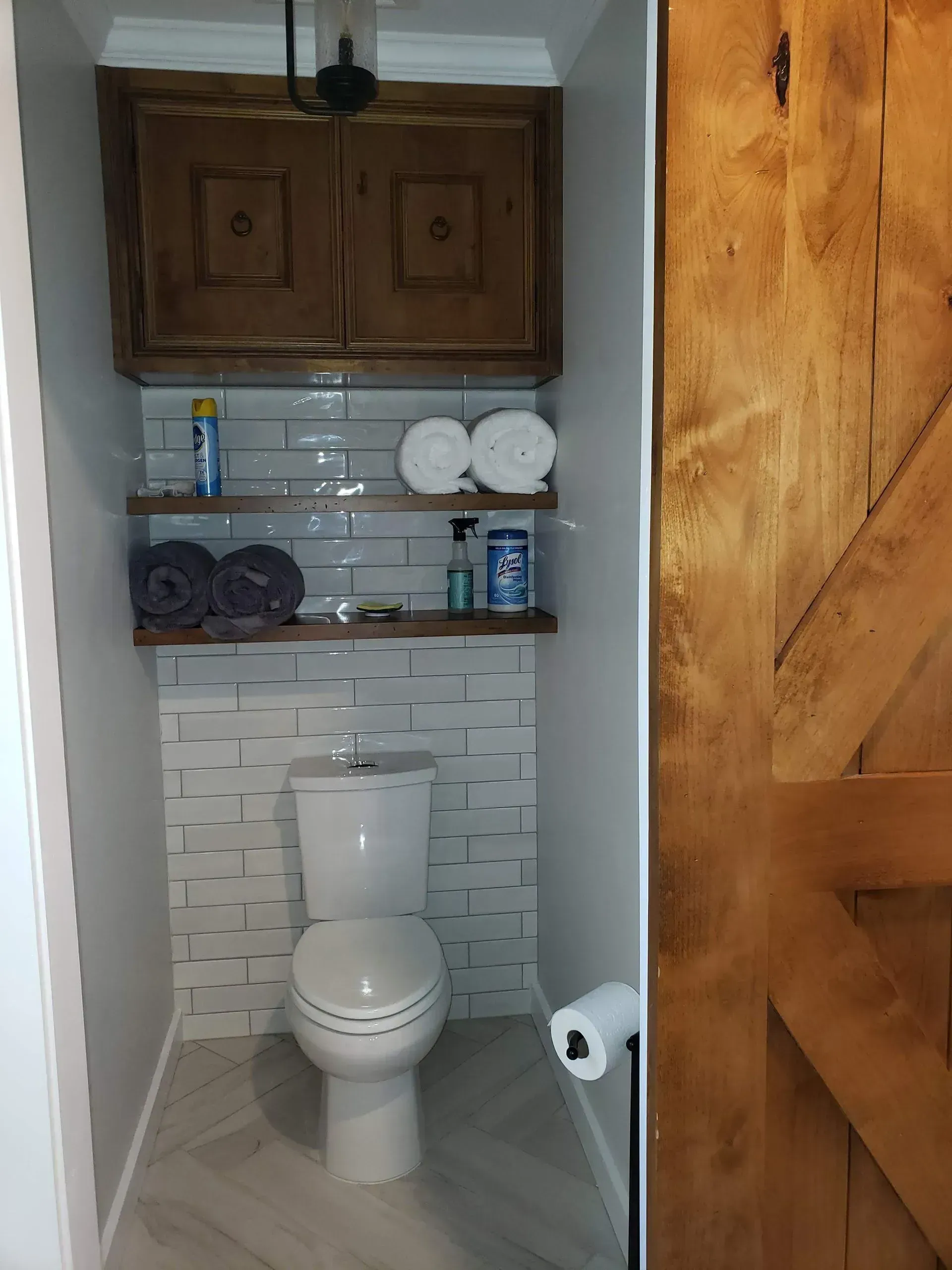 Small bathroom with a toilet, tiled walls, shelves, and an open wooden door.