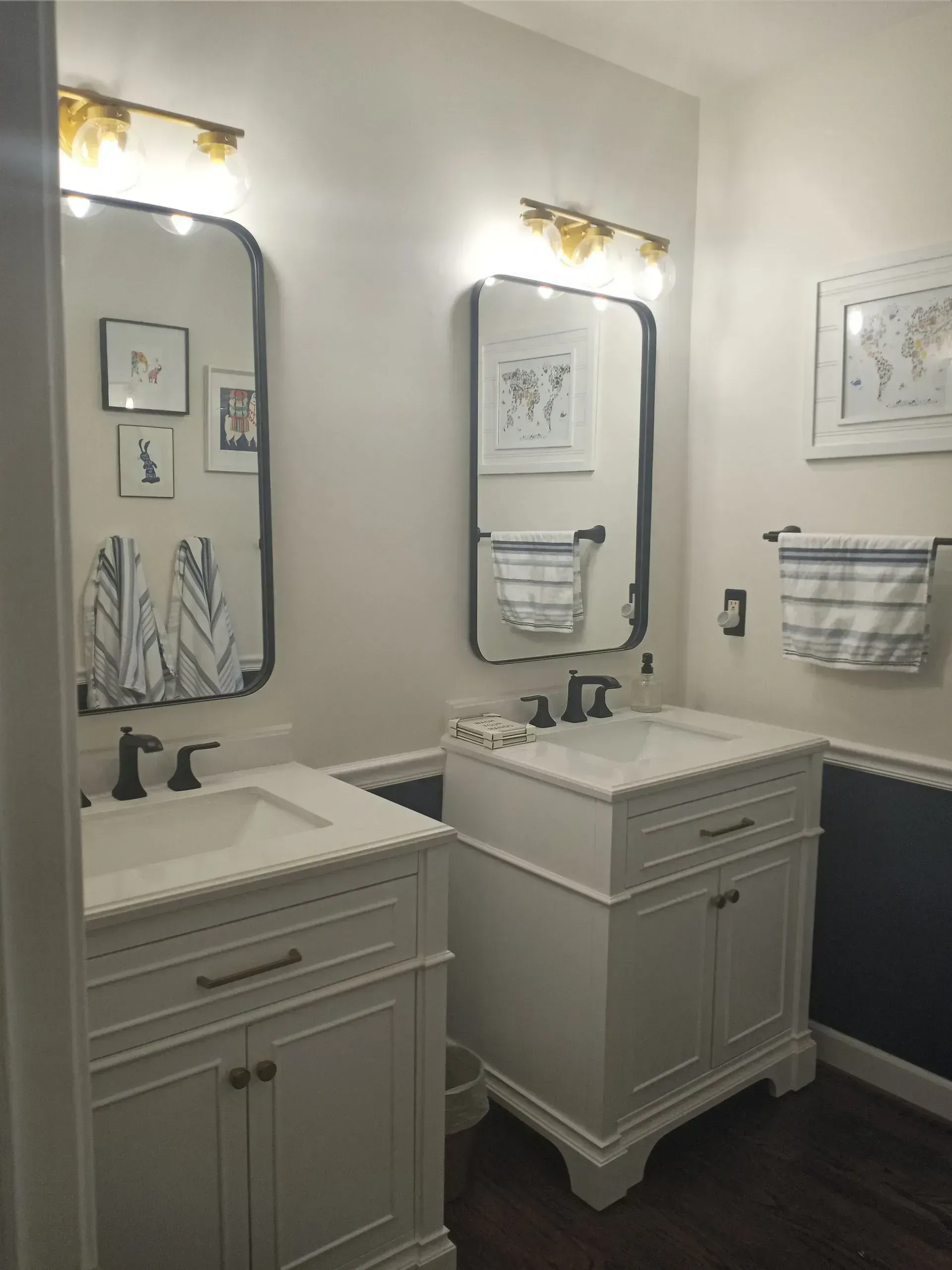 Two mirrored bathroom vanities with white cabinets, marble counters, and lit wall sconces in a bright bathroom.