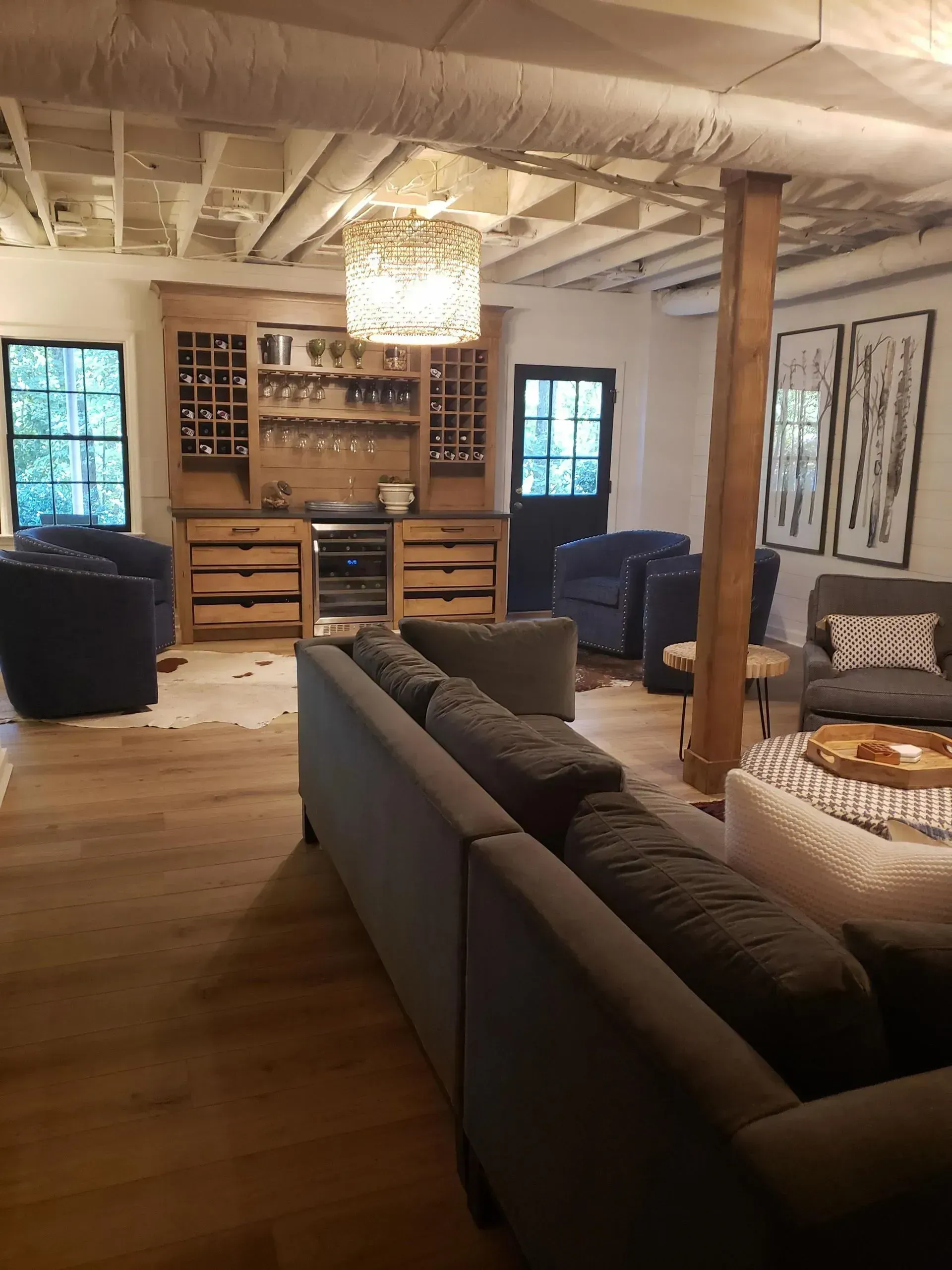 Cozy living room with a gray sectional, fireplace, chandelier, and wood furniture in a rustic basement.