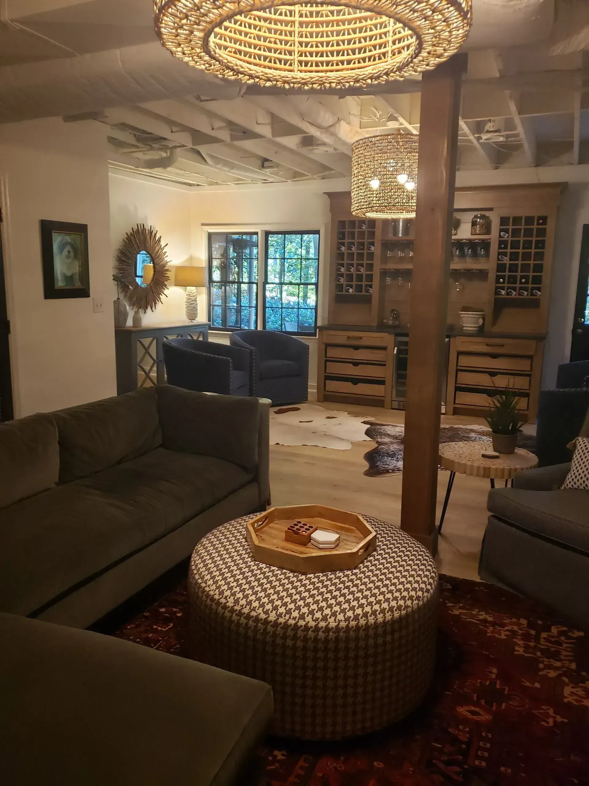 Cozy living room with woven sofas, round ottoman, wooden beam, and hanging chandeliers.