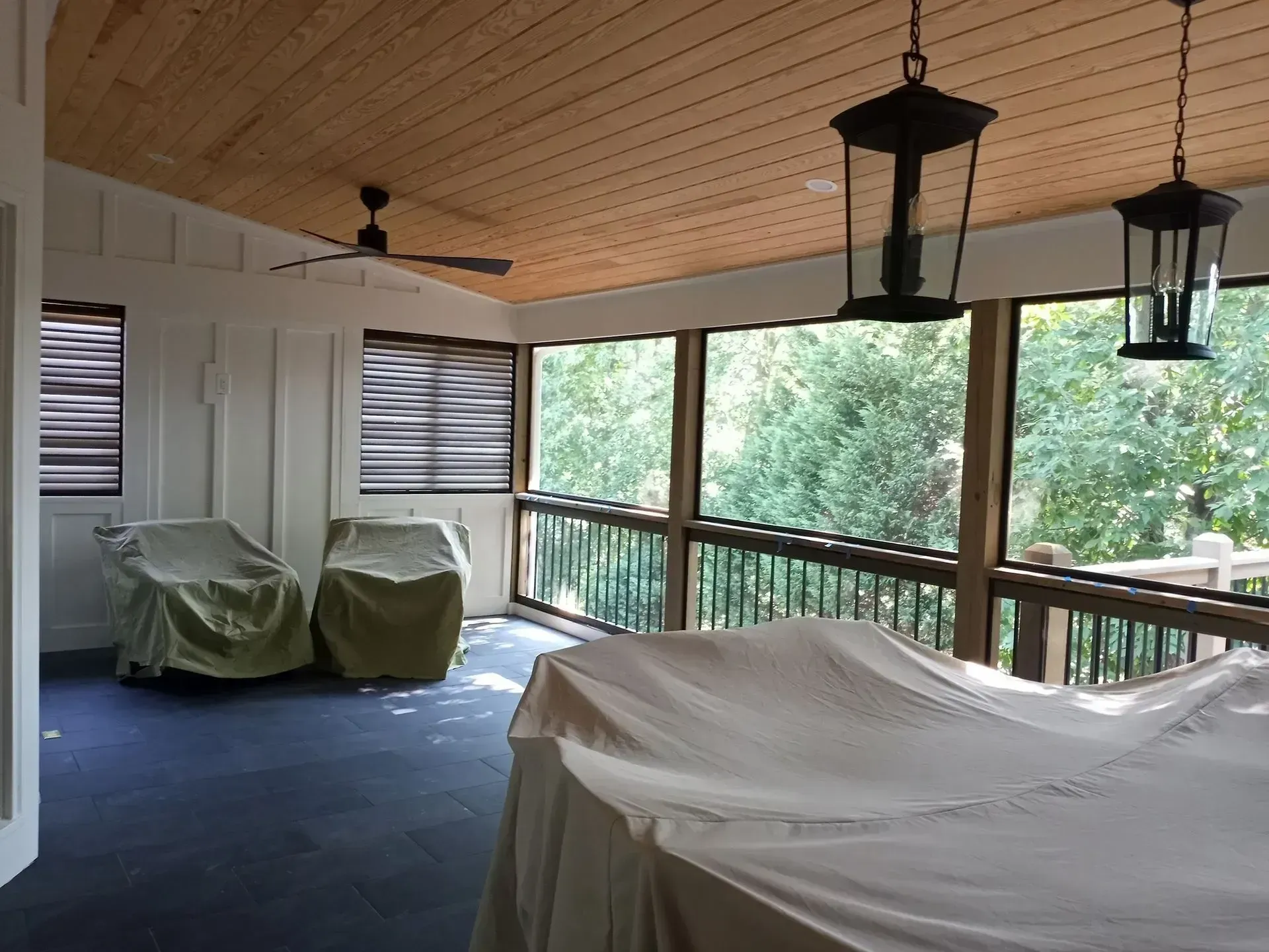 Covered porch with rocking chairs, hanging lanterns, and wooded view beyond the railing.