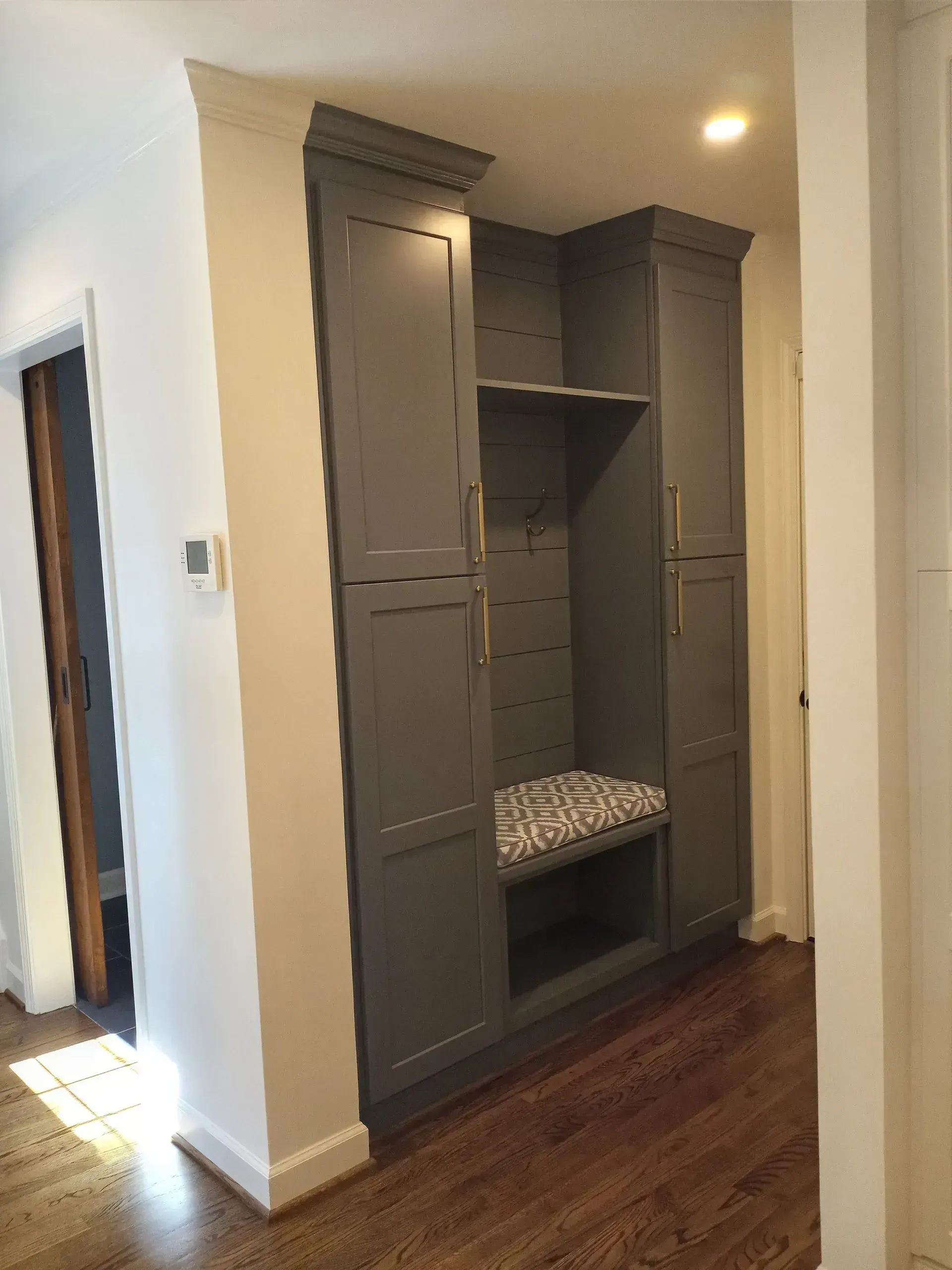 Built-in gray hallway mudroom cabinet with bench, shelves, and drawers on hardwood floor