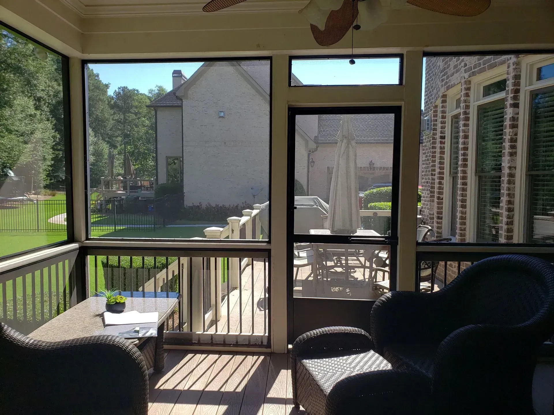 Enclosed porch with railing, chair, small table, and view of neighboring buildings and grassy yard outside