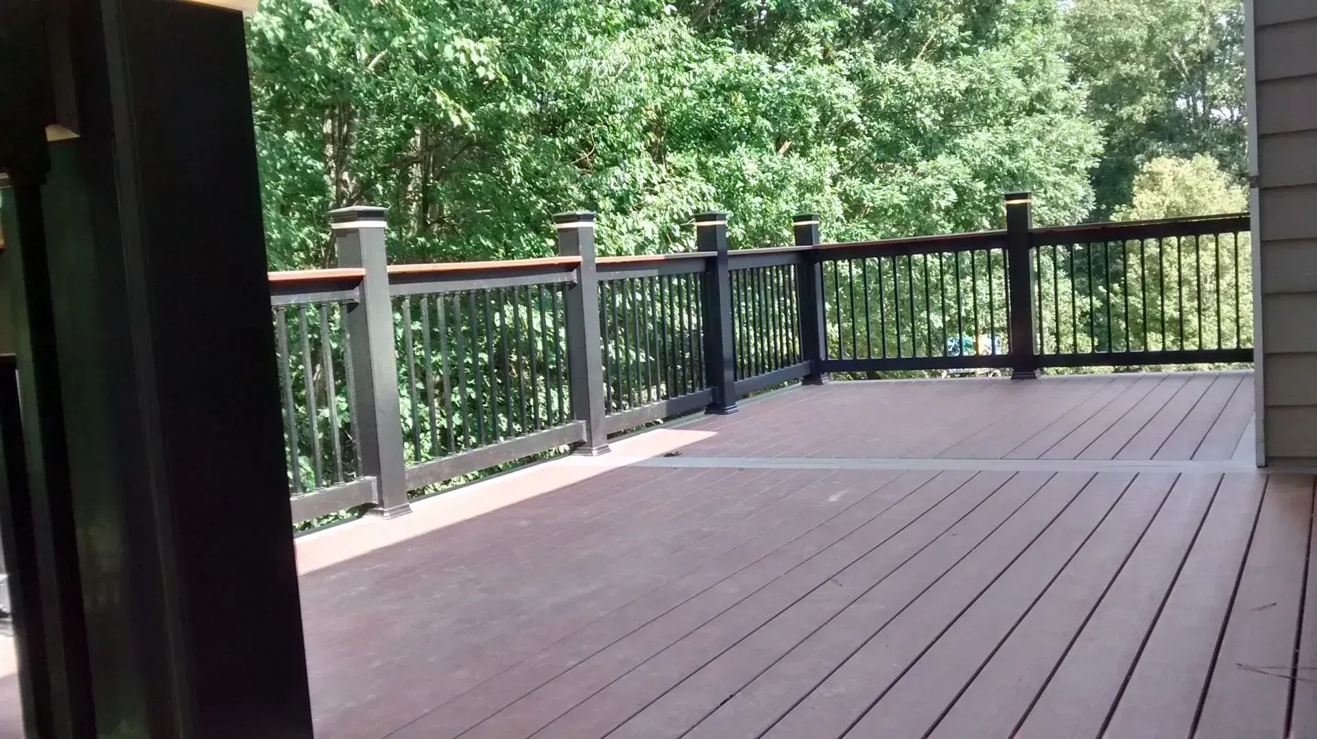 Wooden deck with black railings overlooking green trees and a fenced backyard.