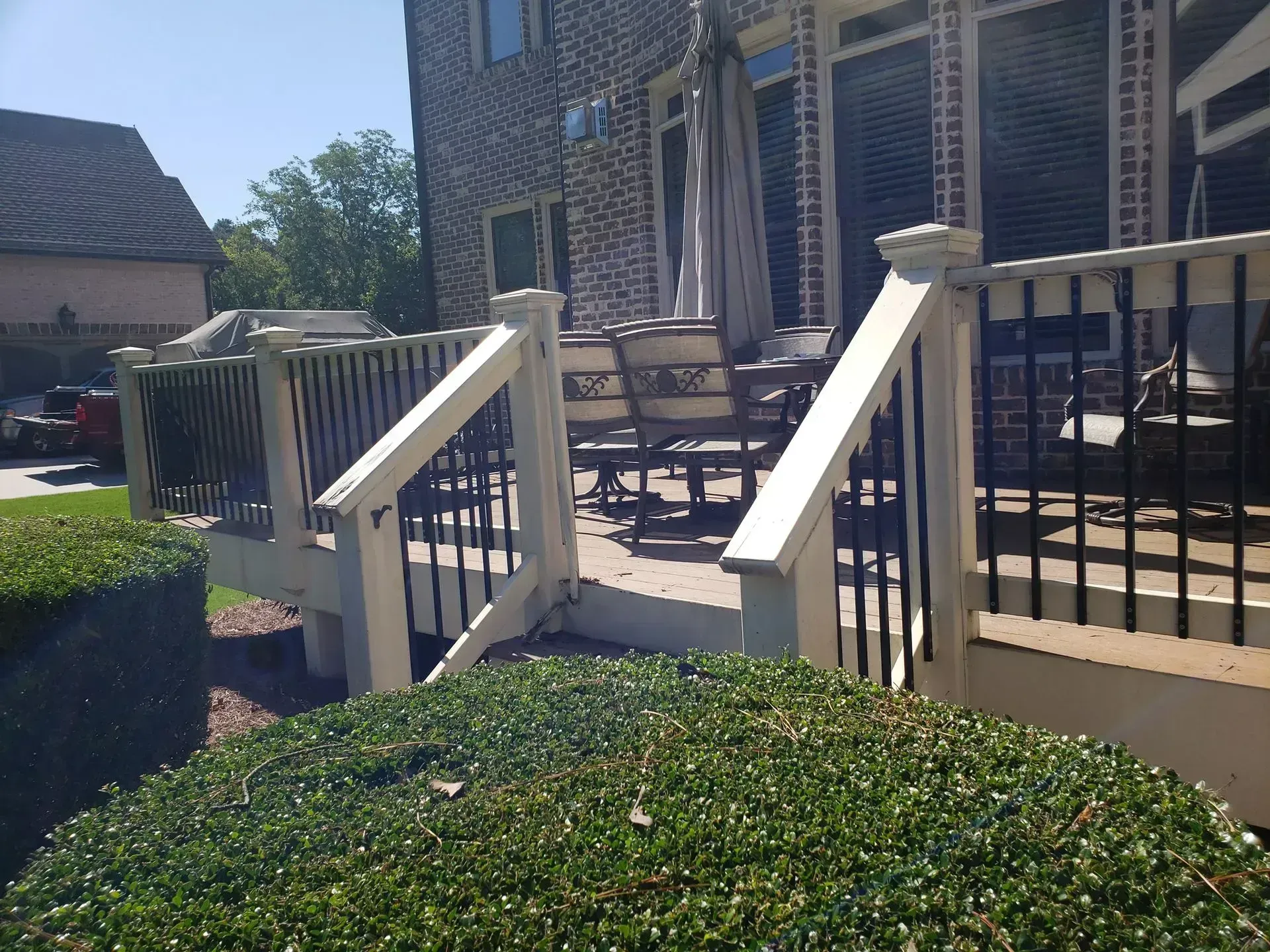 Patio steps with white railings leading to a brick house and outdoor table on a sunny day