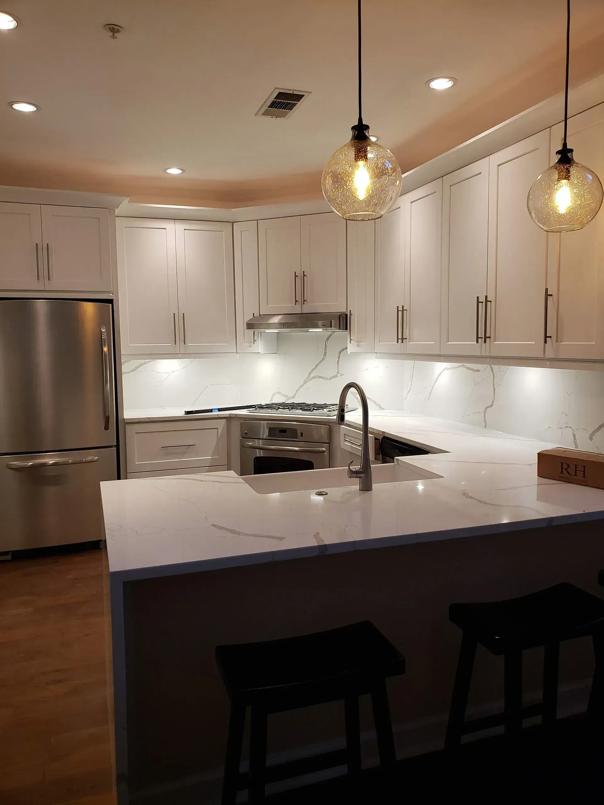 Modern white kitchen with marble island, stainless fridge, and two pendant lights
