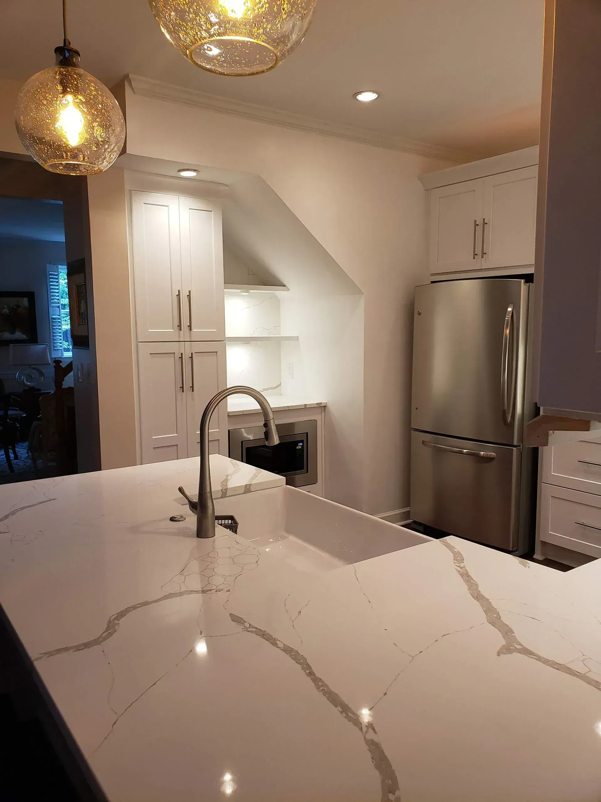 Modern kitchen with white marble island, pendant lights, stainless steel fridge, and white cabinets