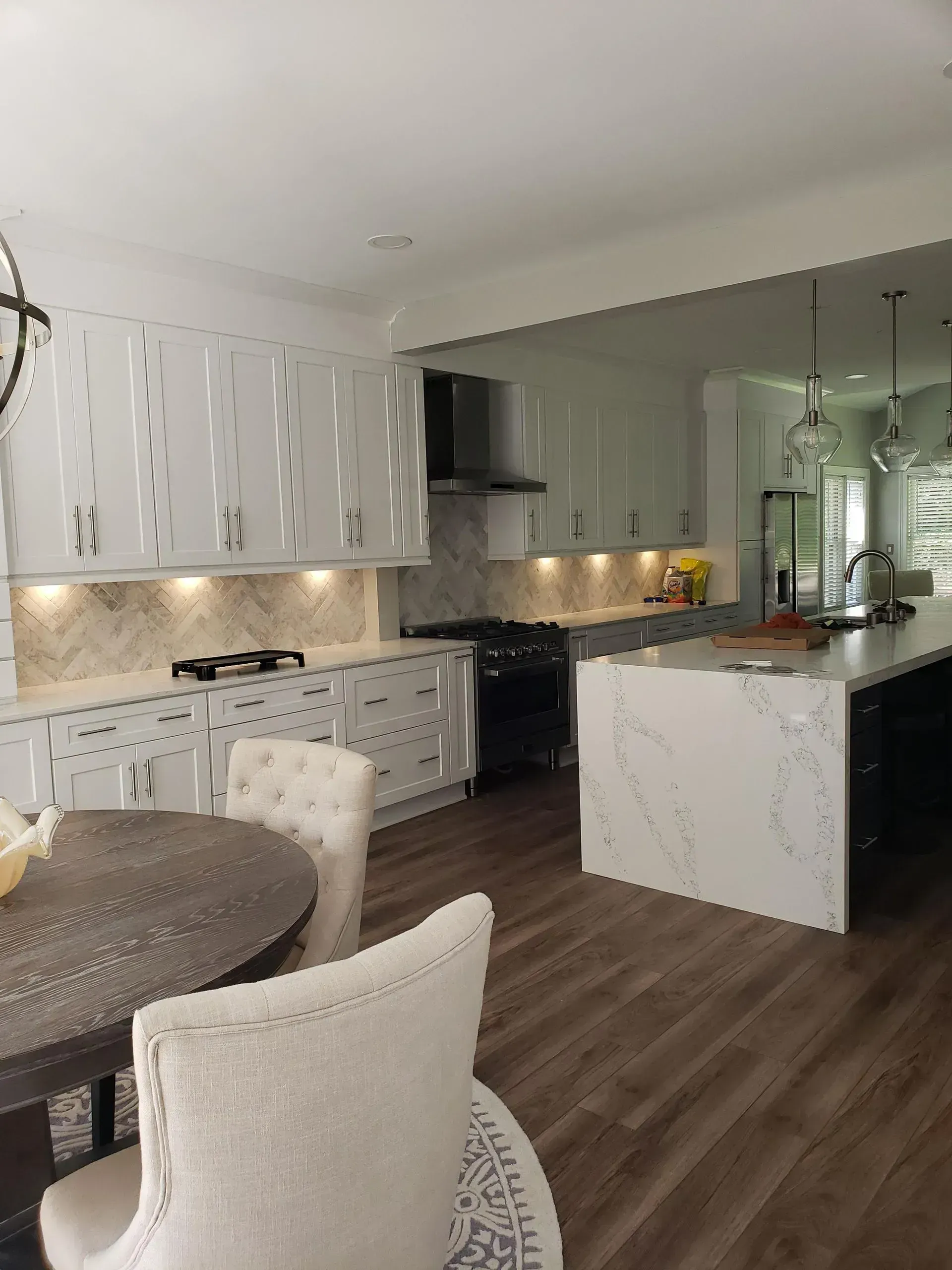 Modern white kitchen and dining area with marble island, dark wood floors, and pendant lights