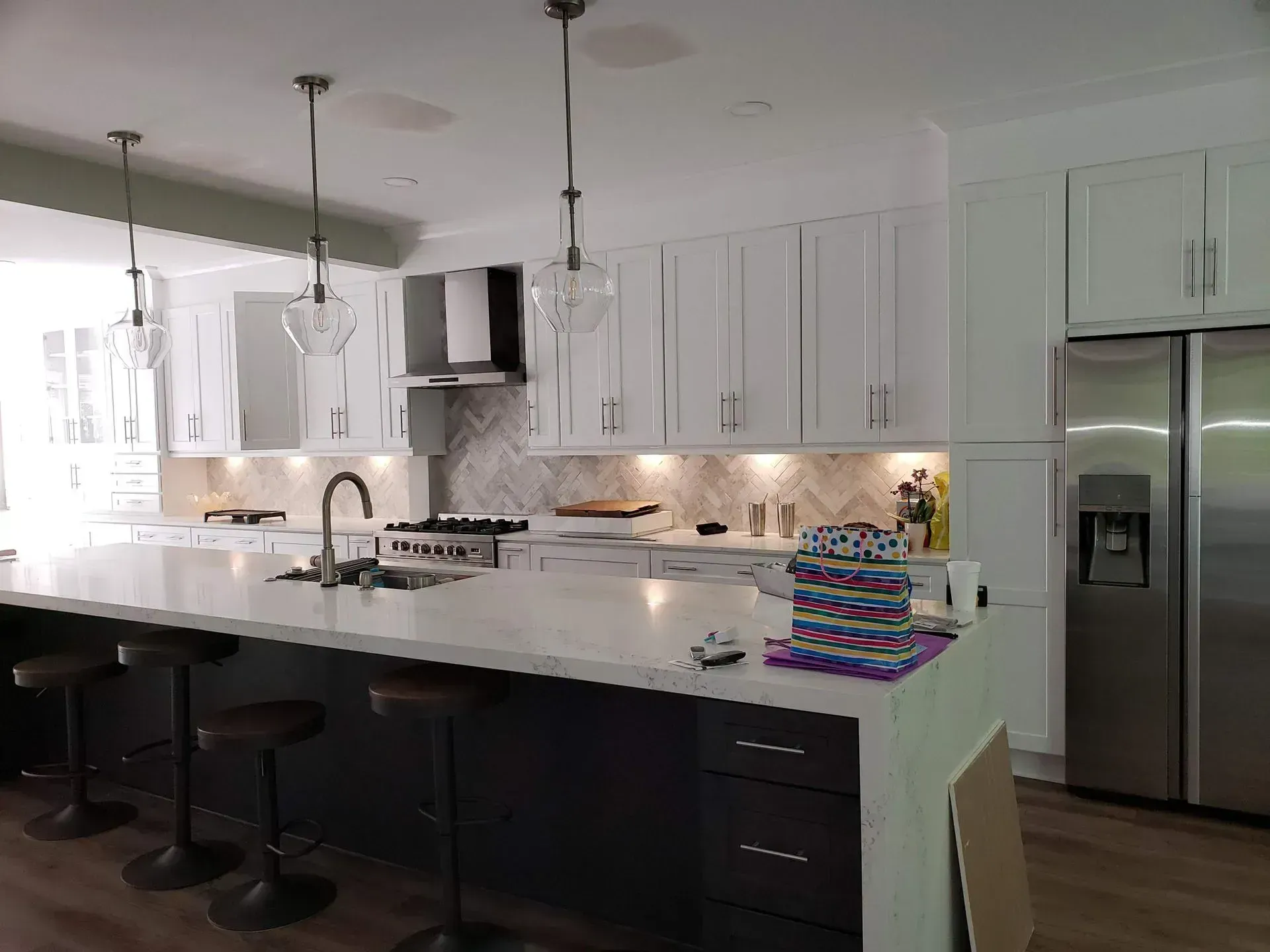 Modern white kitchen with island, bar stools, pendant lights, and stainless steel refrigerator