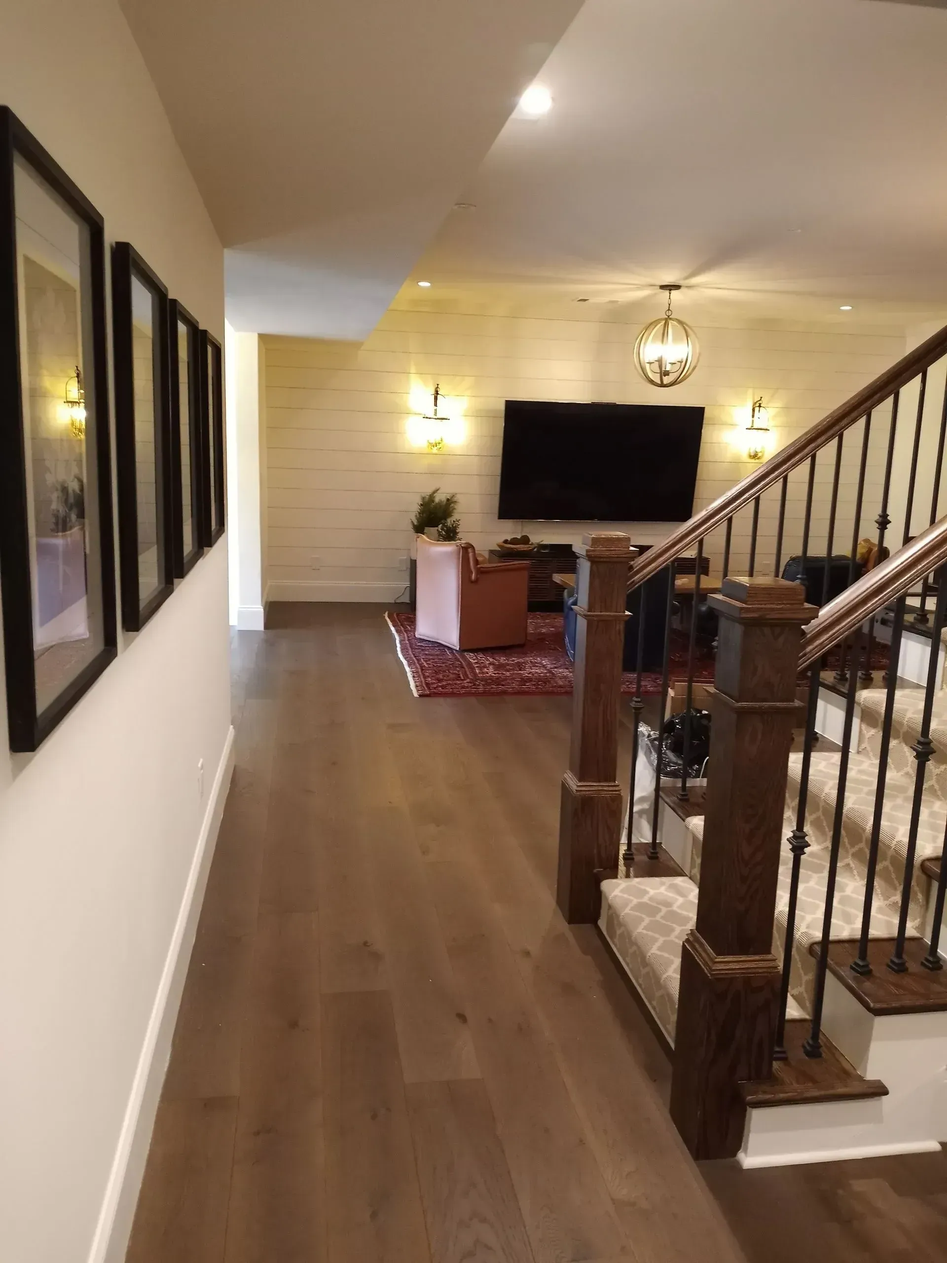 Hallway with wood floors, wall art, staircase, and a living room with TV and red chair.