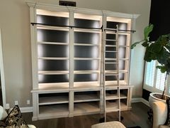 A living room with a large bookshelf and a ladder.
