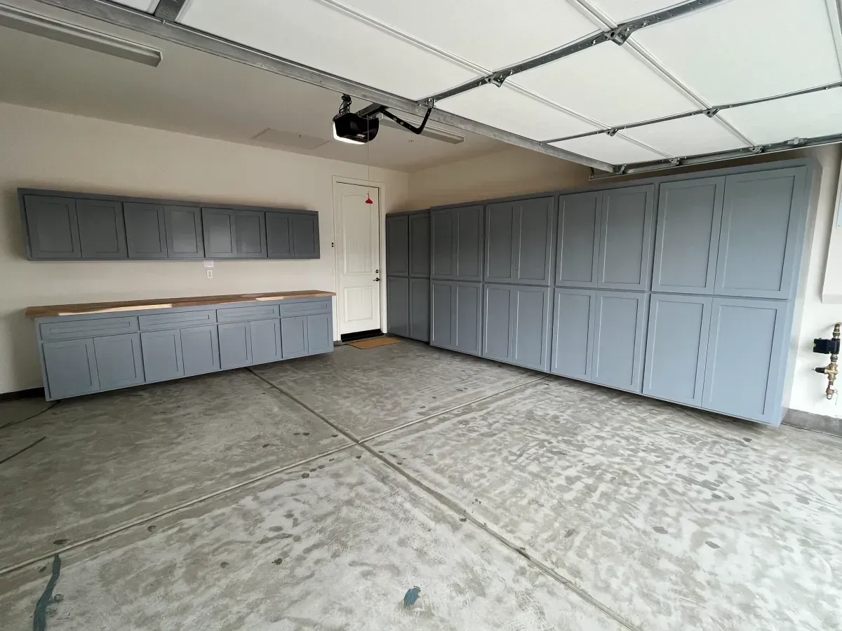 A garage with gray cabinets and a garage door open.