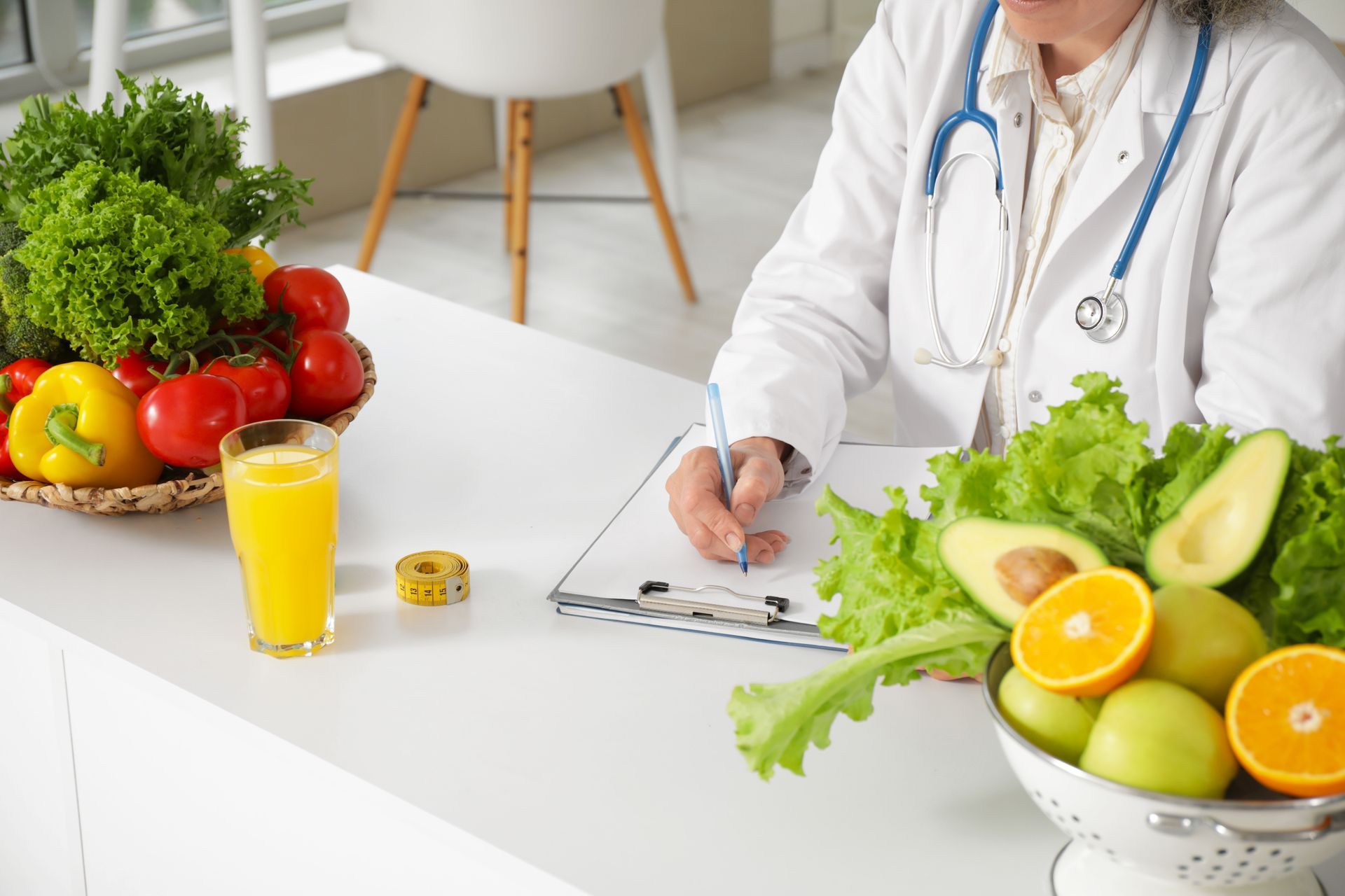 Dietitian in white coat writing, surrounded by vegetables and fruit on a white table.