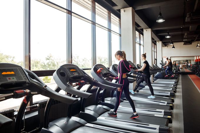 People exercising on treadmills in a bright gym with large windows