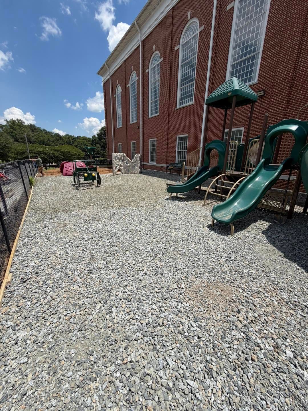 Gravel courtyard beside a red brick building with green playground slides under a blue sky