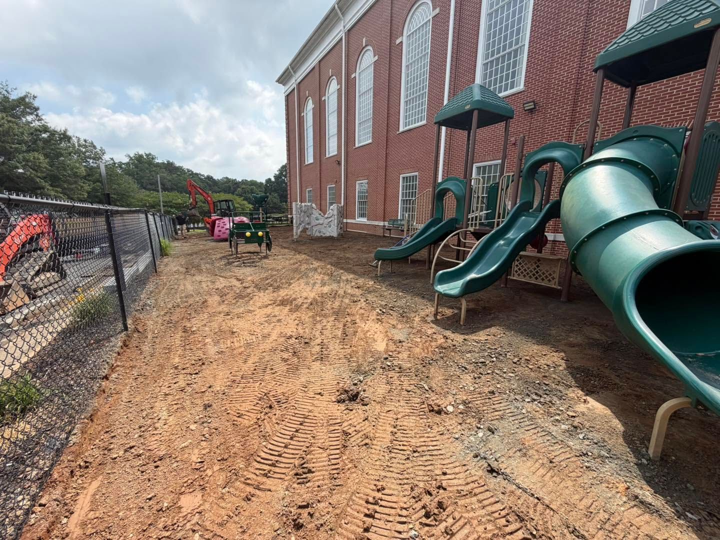 Brick building beside playground with green slides and muddy ground after rain